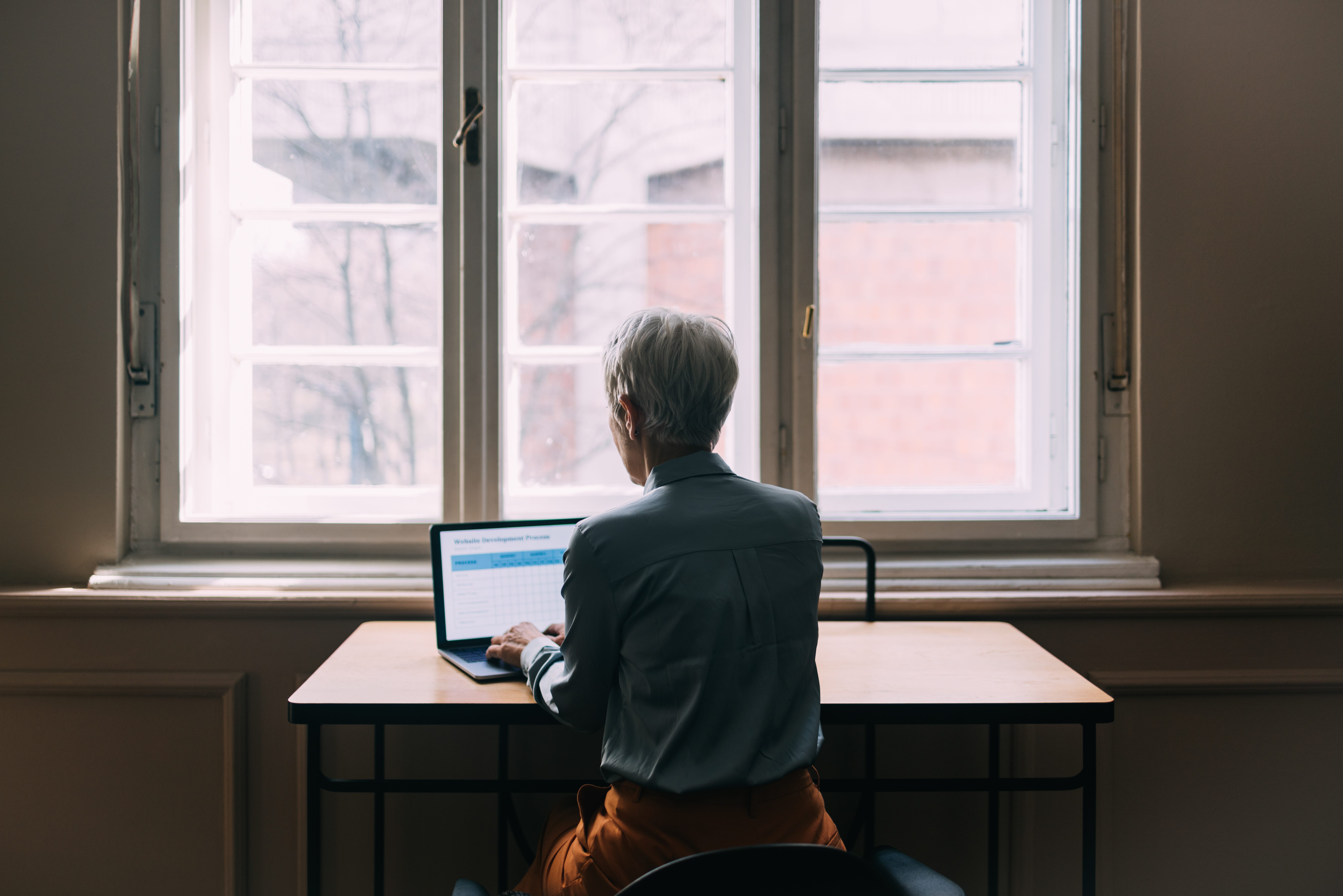 Rear view of old woman working in the window