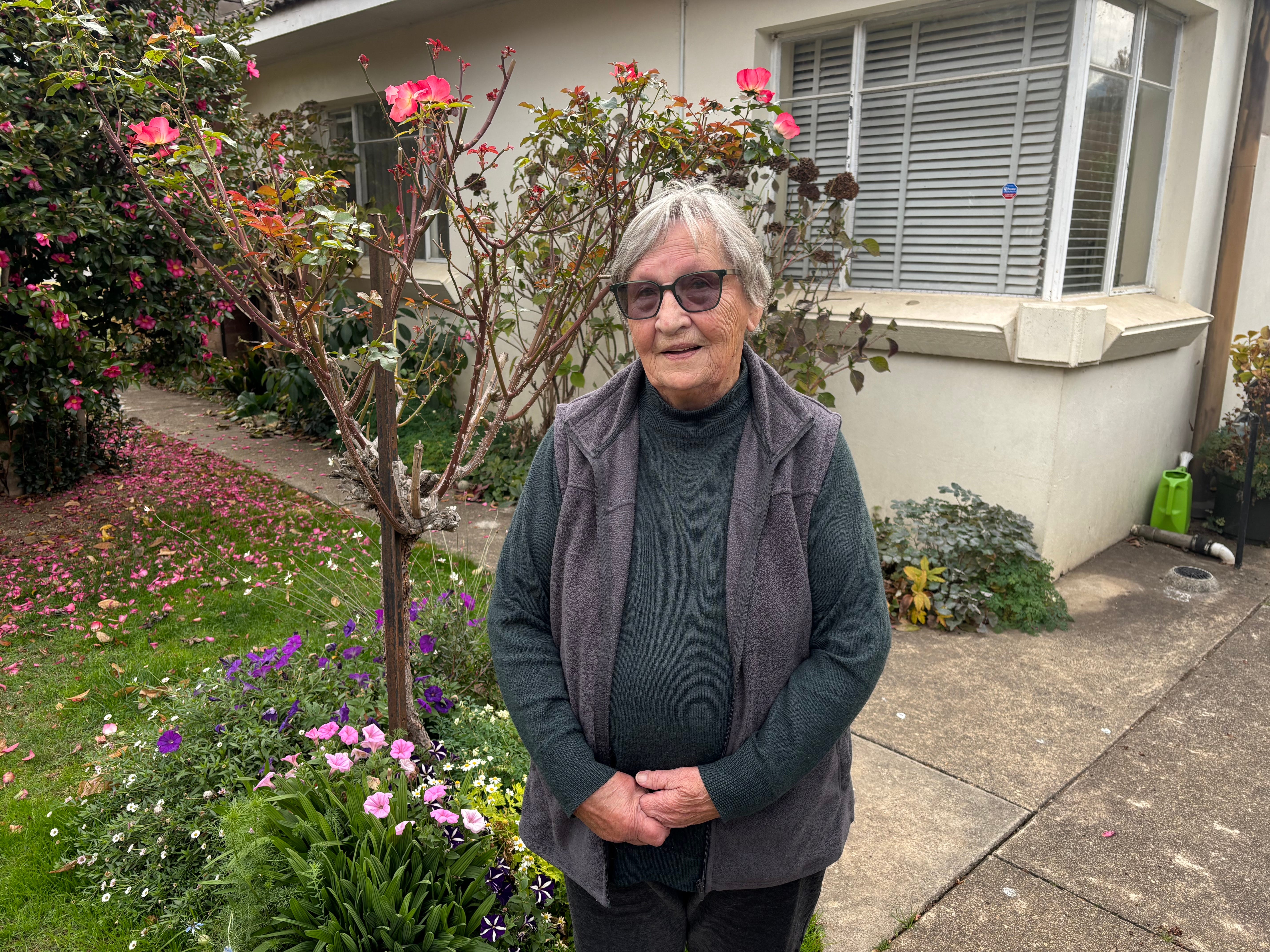 Mira Armstrong wearing sunglasses and standing in front of flowers in front of her house.