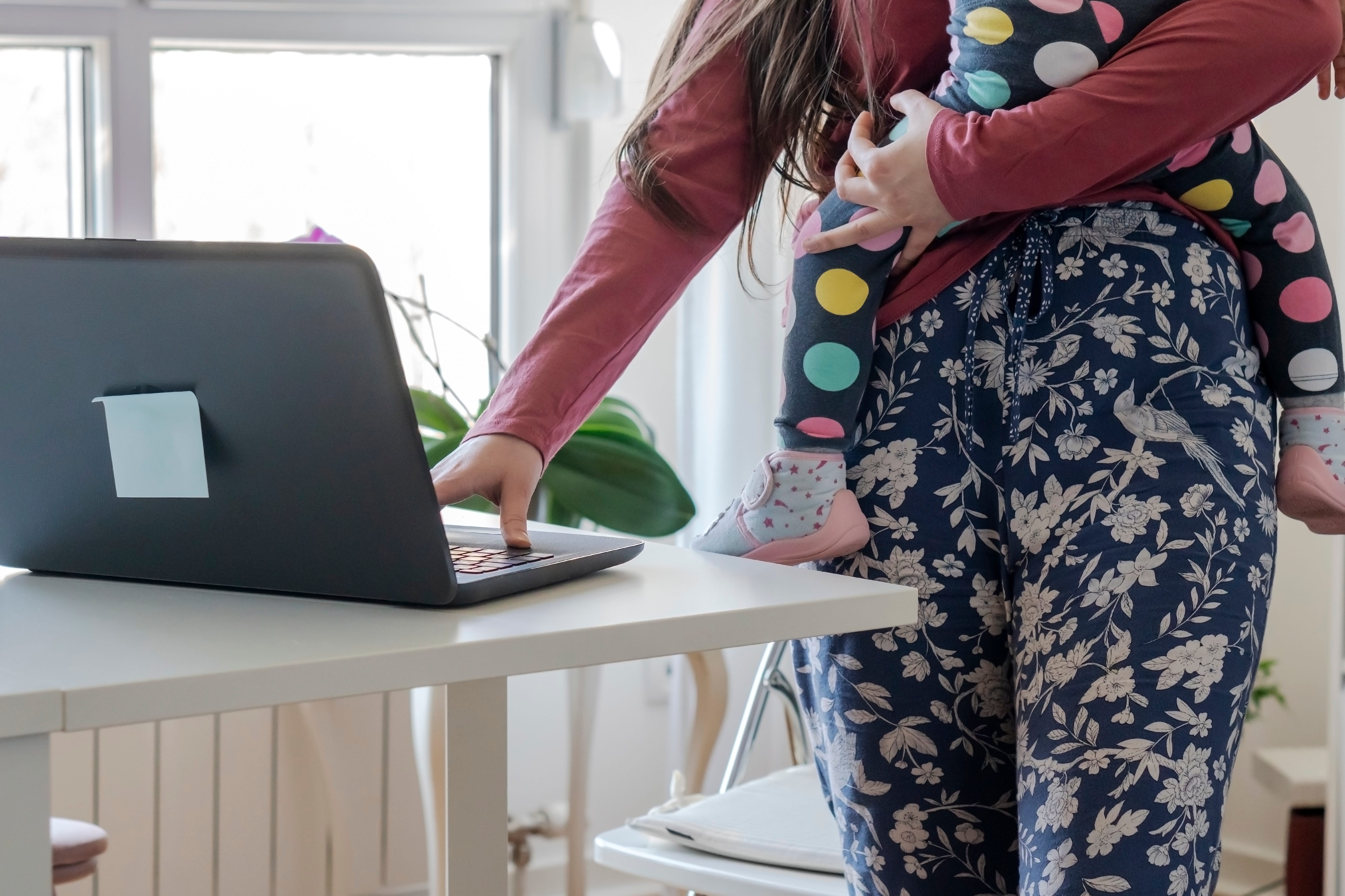 Single mother holding her little daughter and using a laptop.