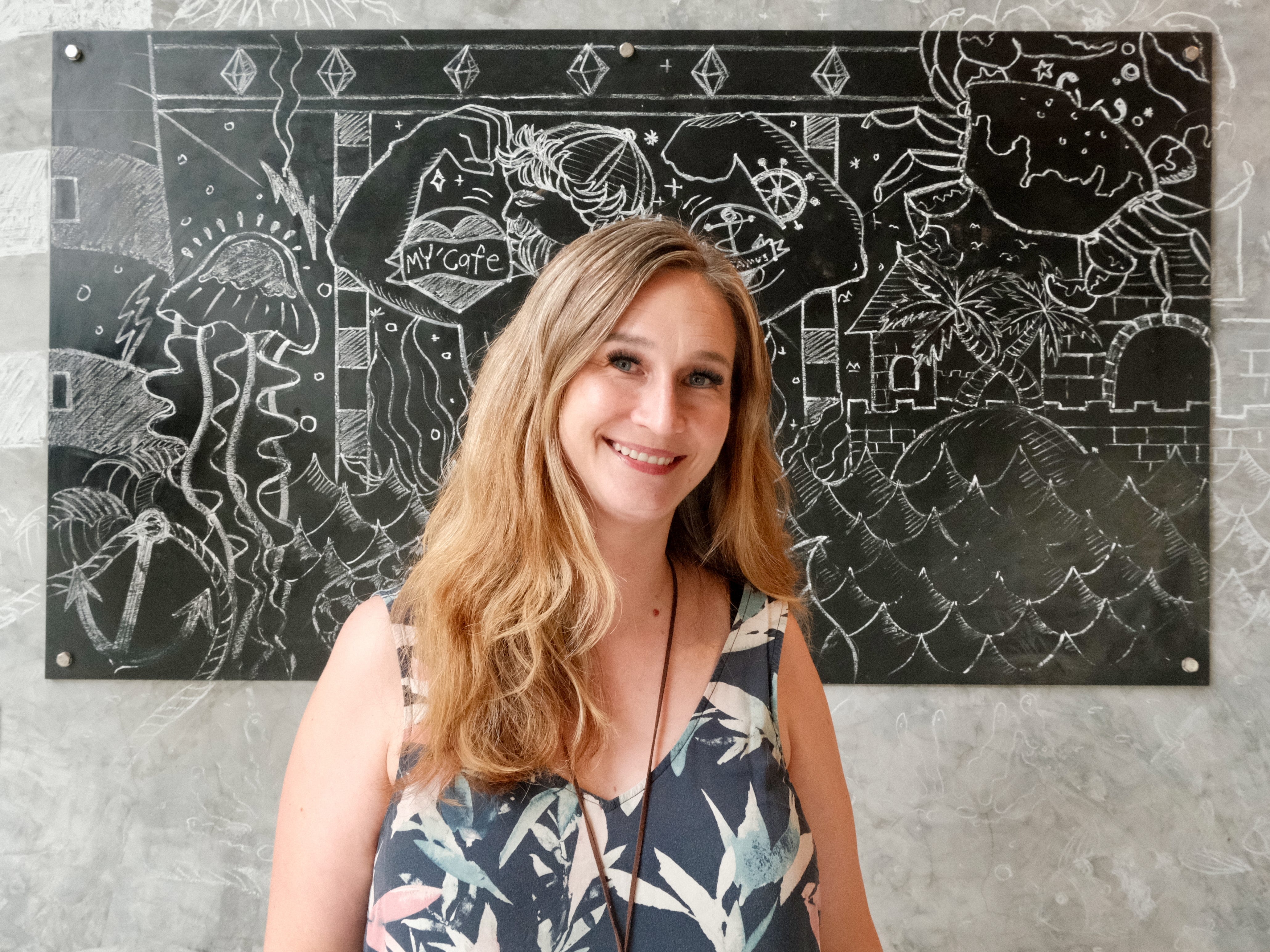 A Caucasian woman posing for a photo in front of a painting in a café in Koh Samui, Thailand.