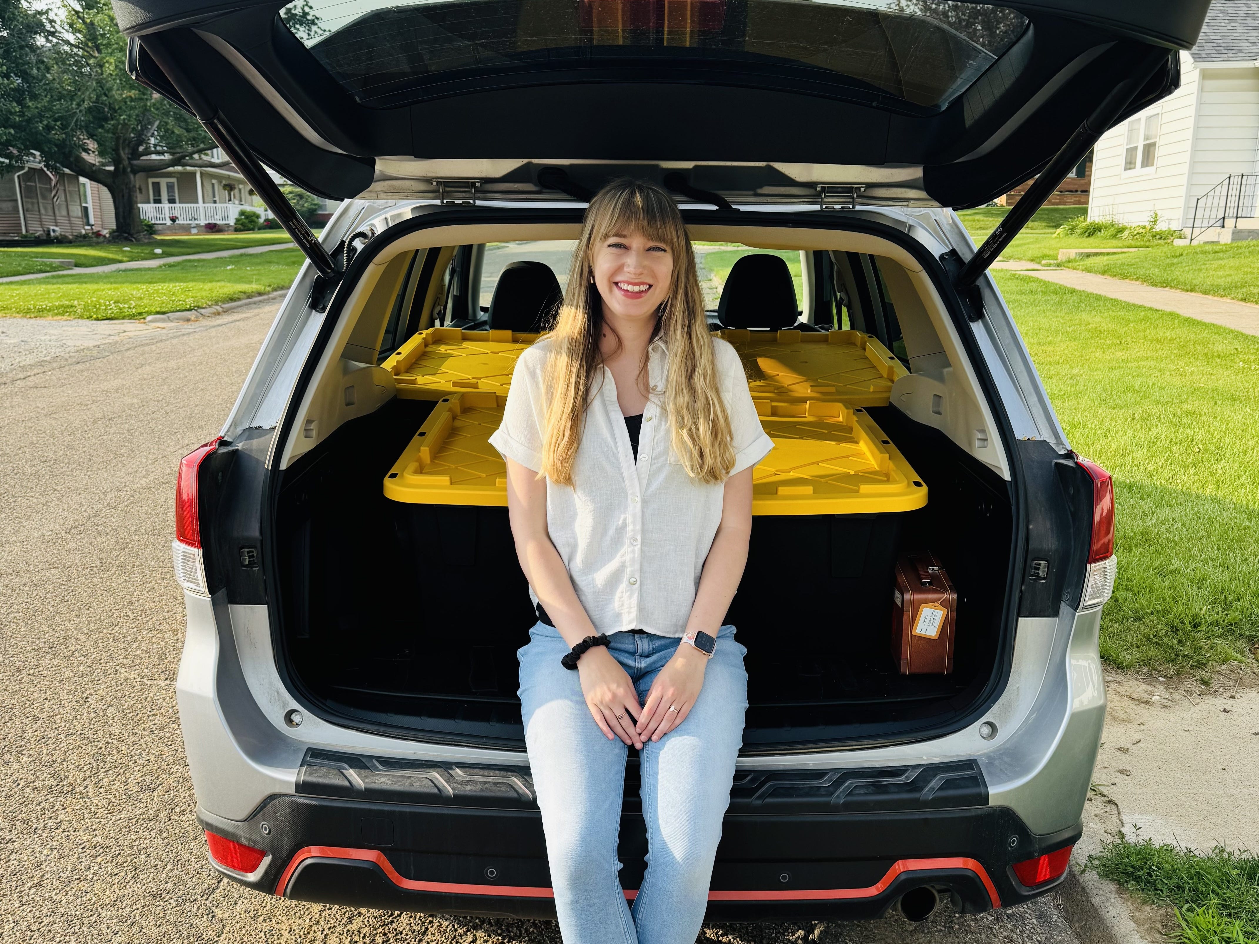 Emily sits in the open trunk of her SUV, with storage bins packed in behind her.
