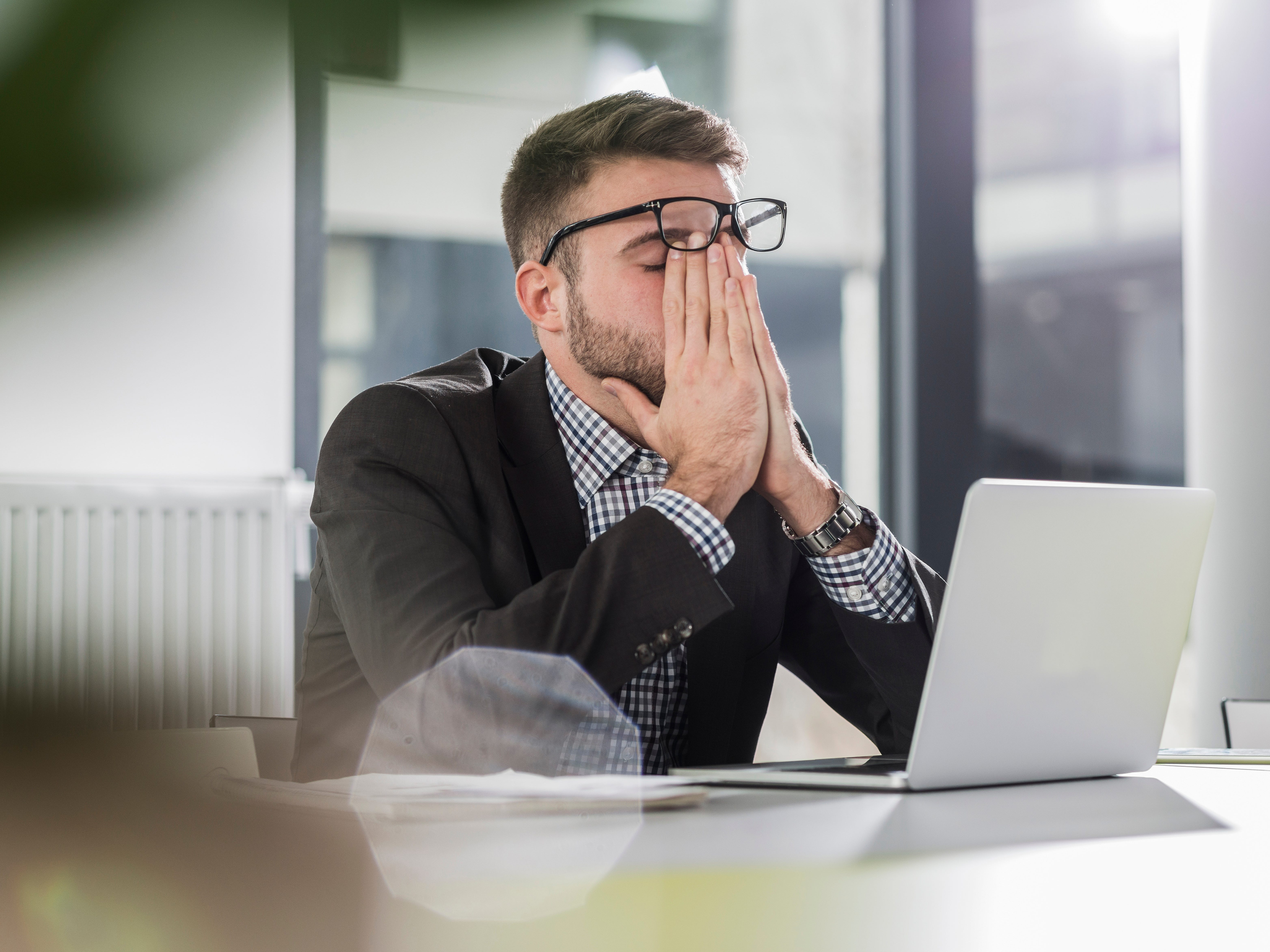 A person sitting in a building next to a laptop with his hands on his face