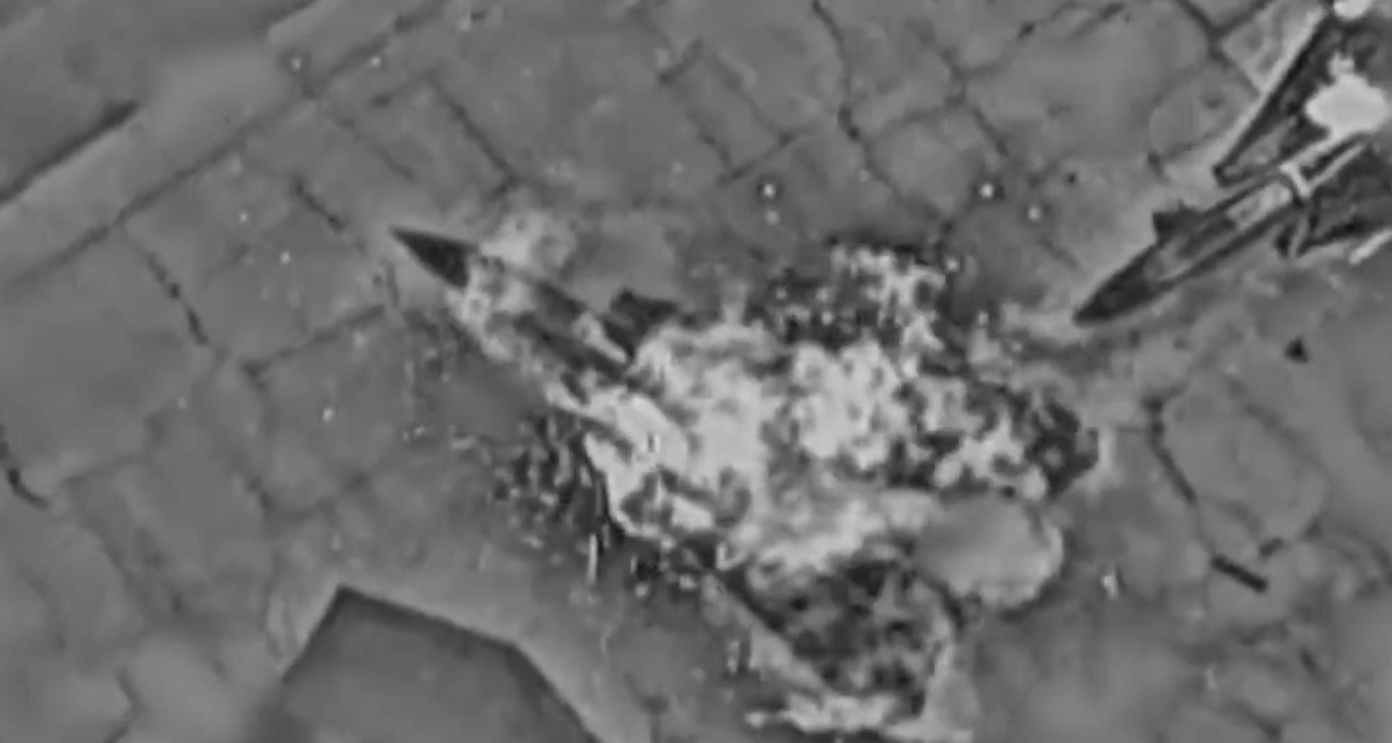 A black-and-white footage still shows what appears to be flames on a jet in an aerial view