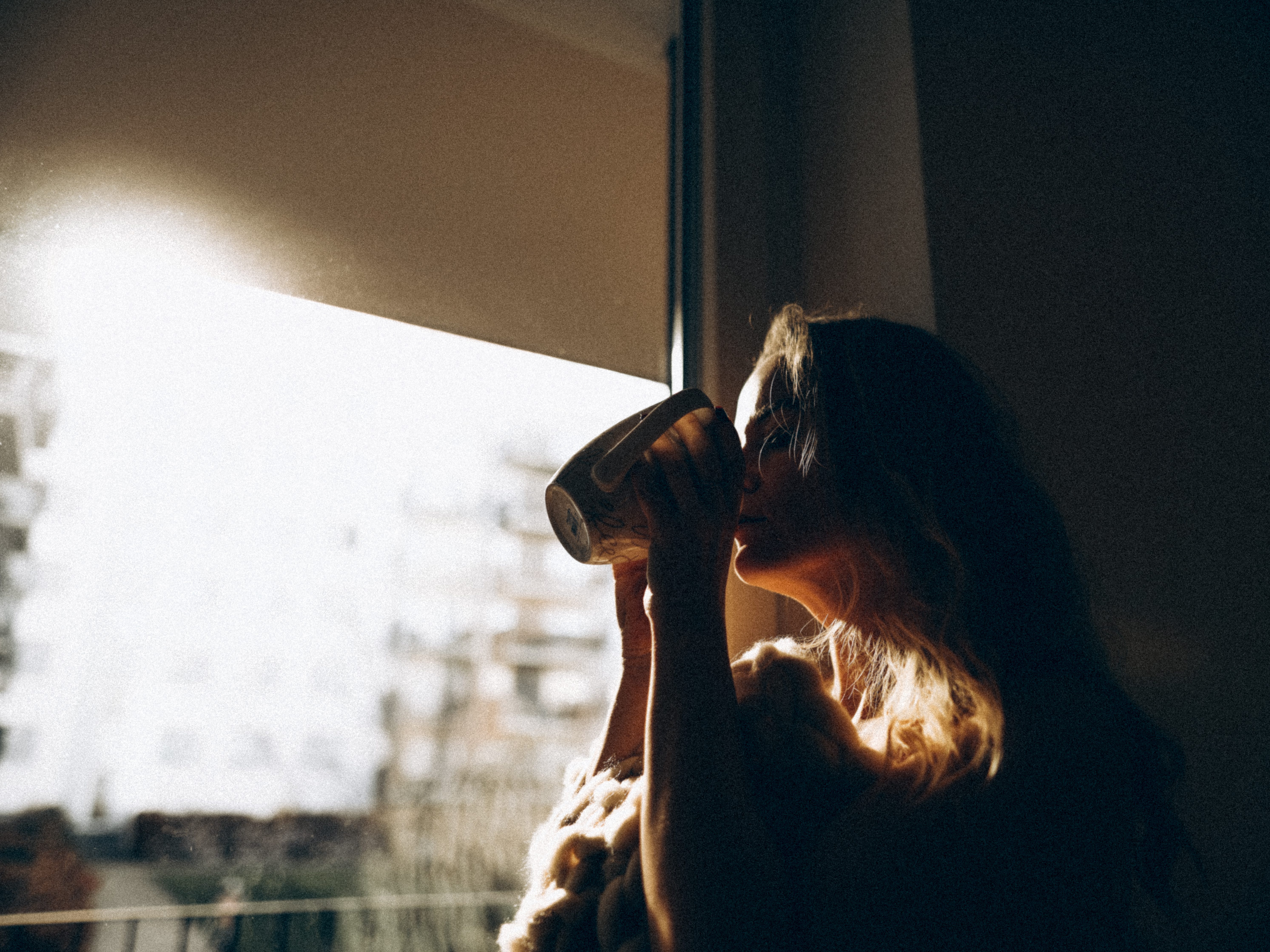 A woman drinking coffee as the sun rises.