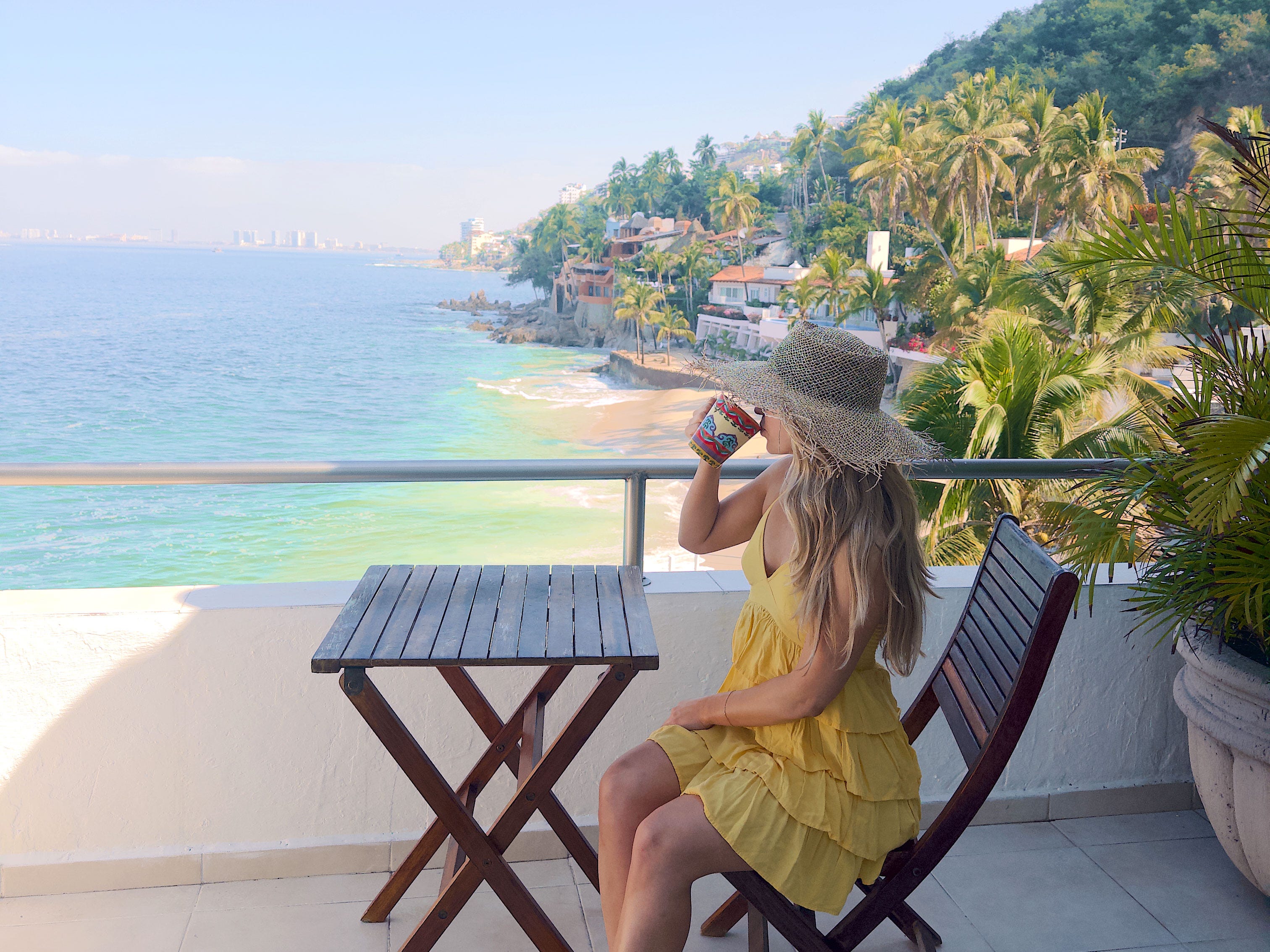 Chloe sips a drink on a patio overlooking a beach.