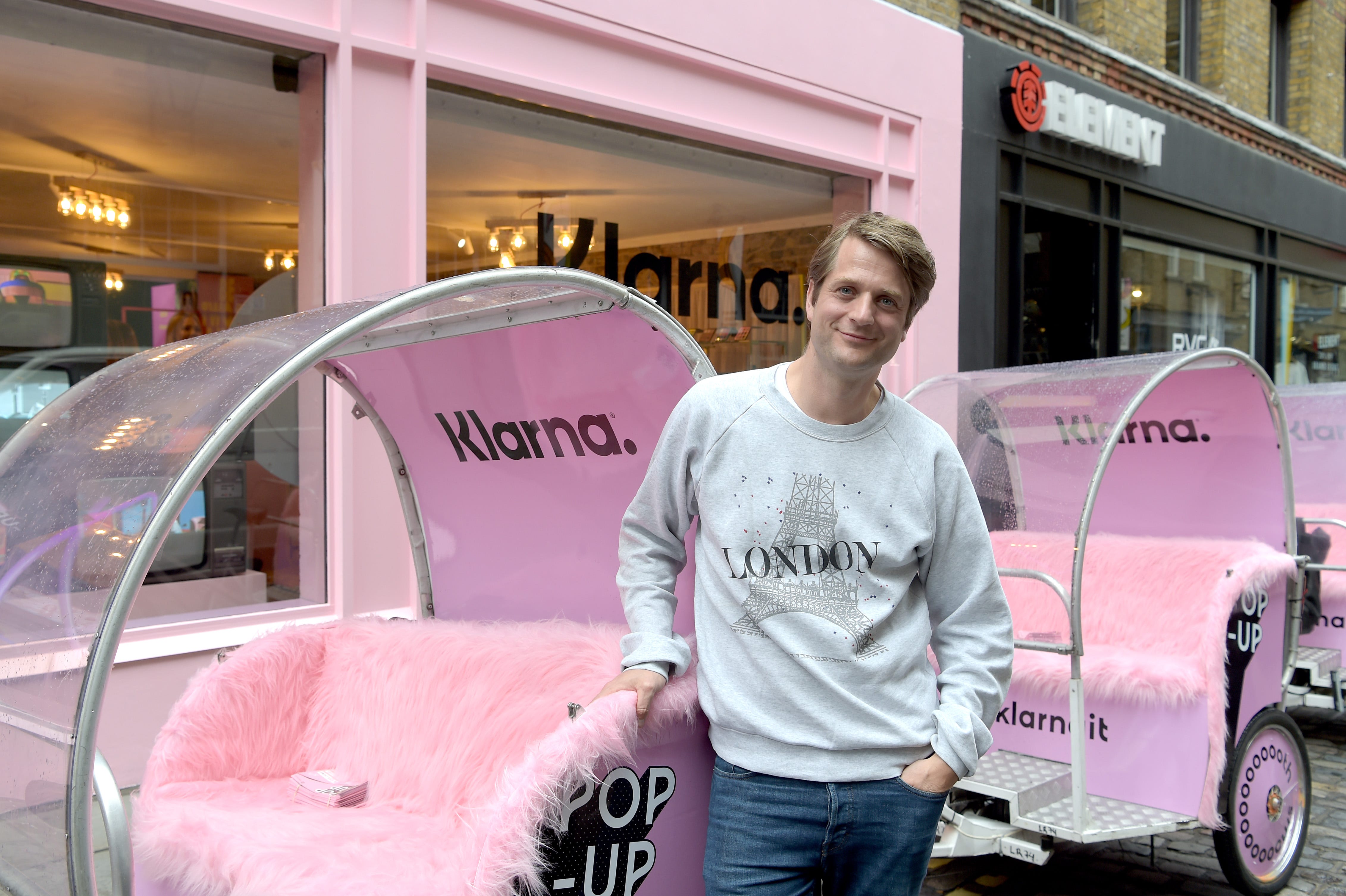 Klarna CEO Sebastian Siemiatkowski smiles whilst wearing a gray sweatshirt and blue jeans and posing near Klarna's pop up store in London.