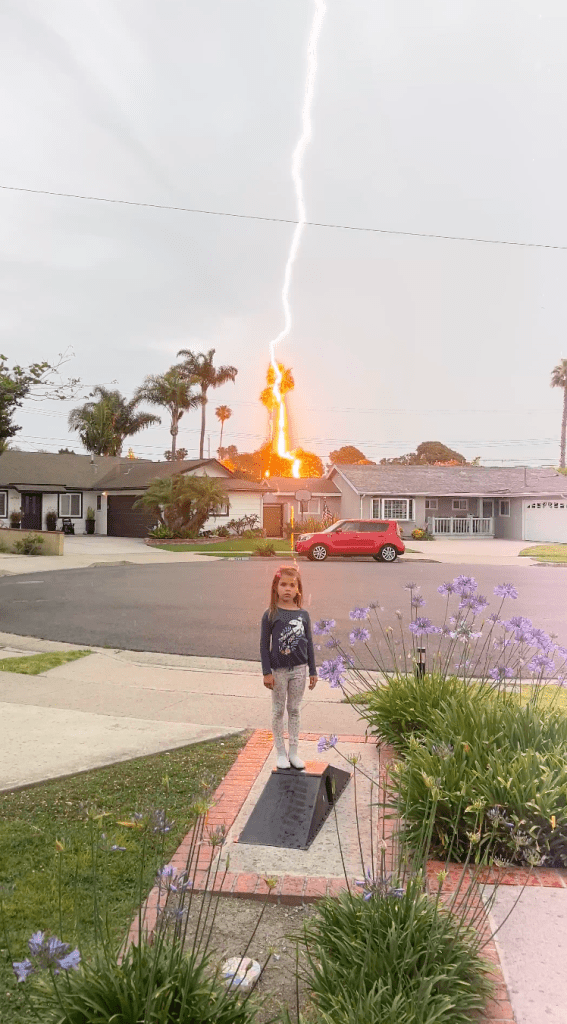 Tiffanie Buckner's daughter Penelope stands outside their Southern California home as lightning strikes a tree behind her.