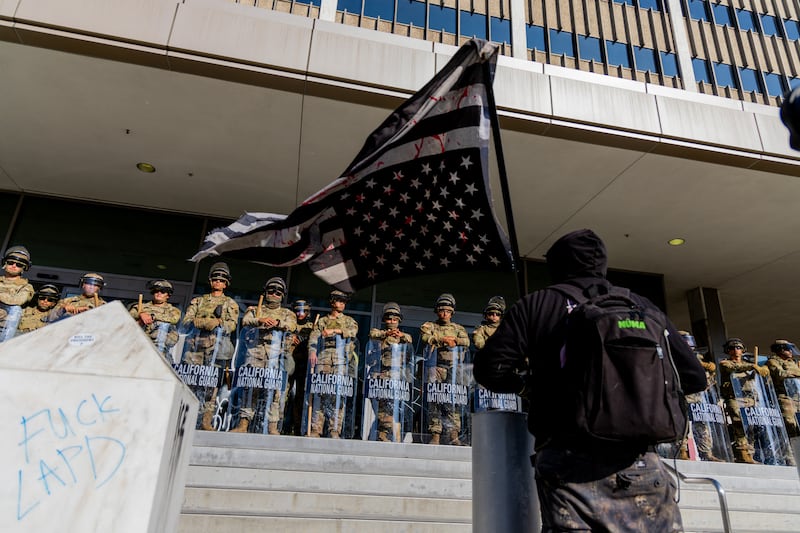 A protester waves an upside-down American flag in front of members of the California National Guard before a curfew takes effect in Los Angeles