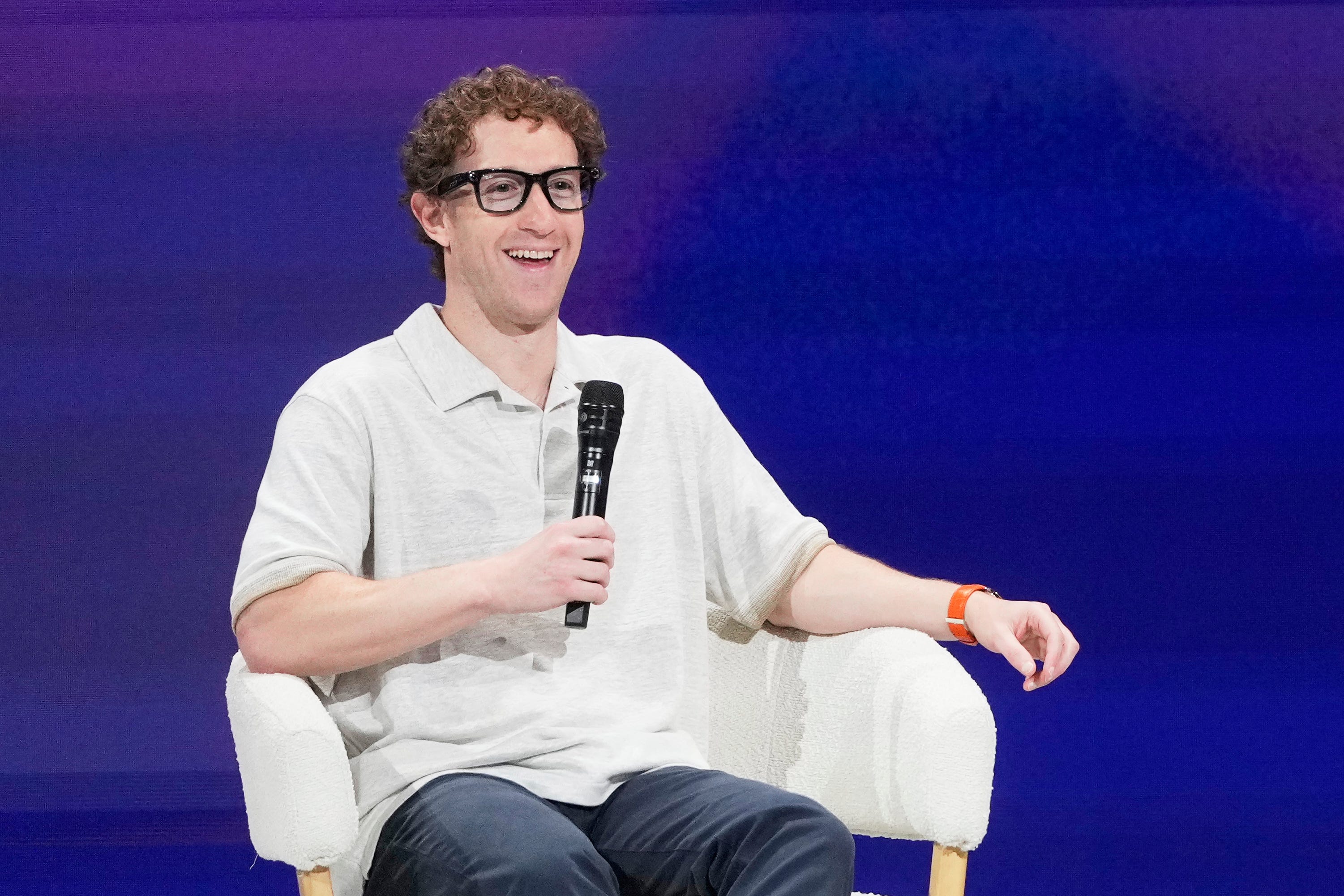 Mark Zuckerberg sits and holds a microphone at LlamaCon.