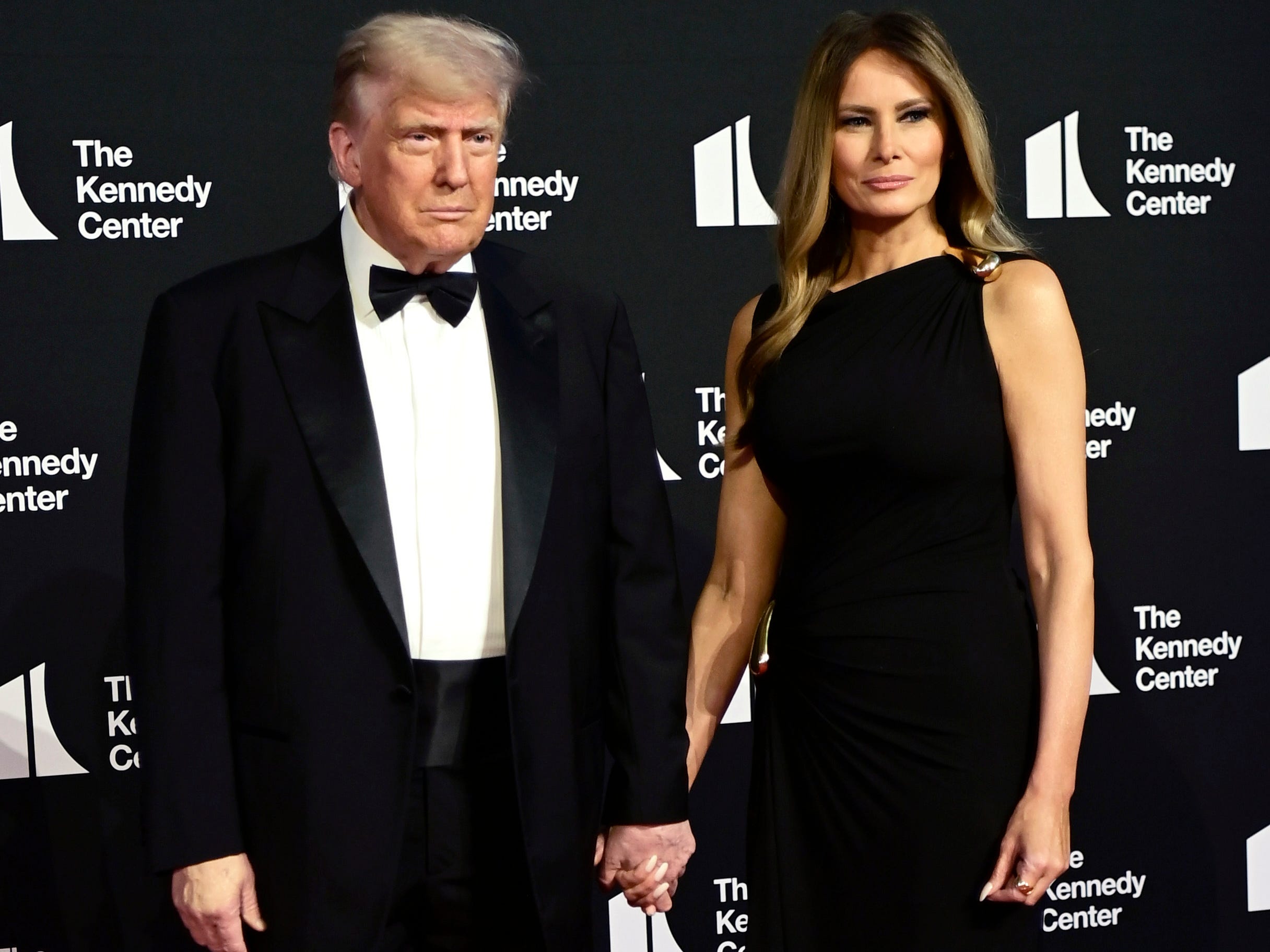 Donald and Melania Trump hold hands on a red carpet at the Kennedy Center.