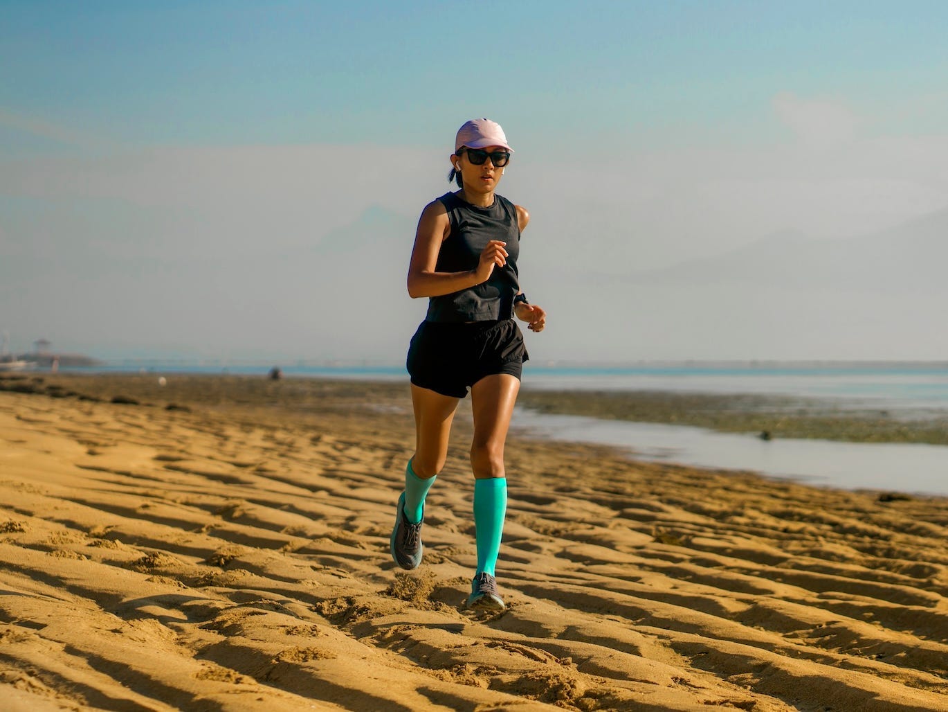 A woman running on a beach in compression socks.