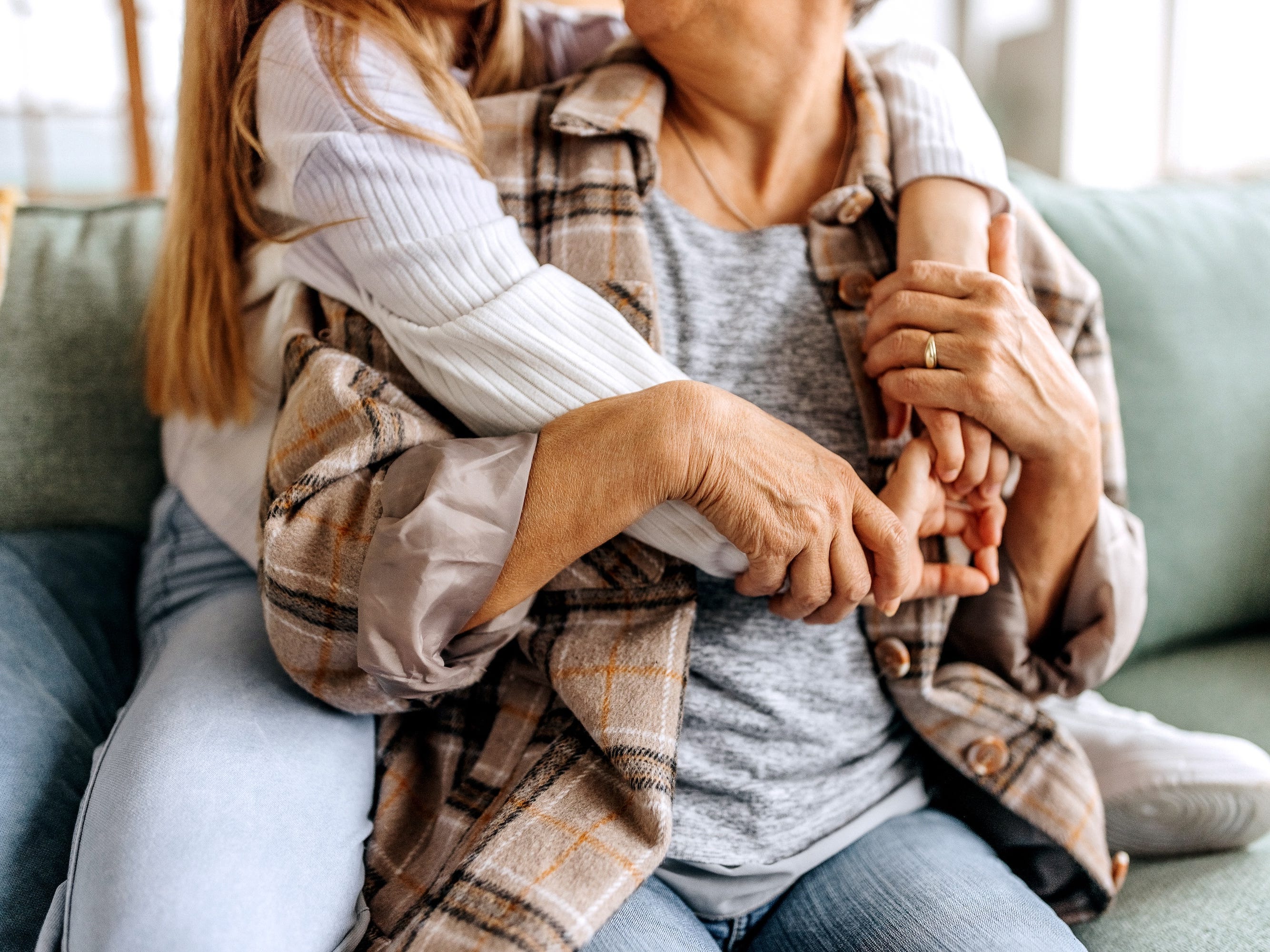 Teenage girl sitting behind older woman and hugging her while sitting on light green couch.