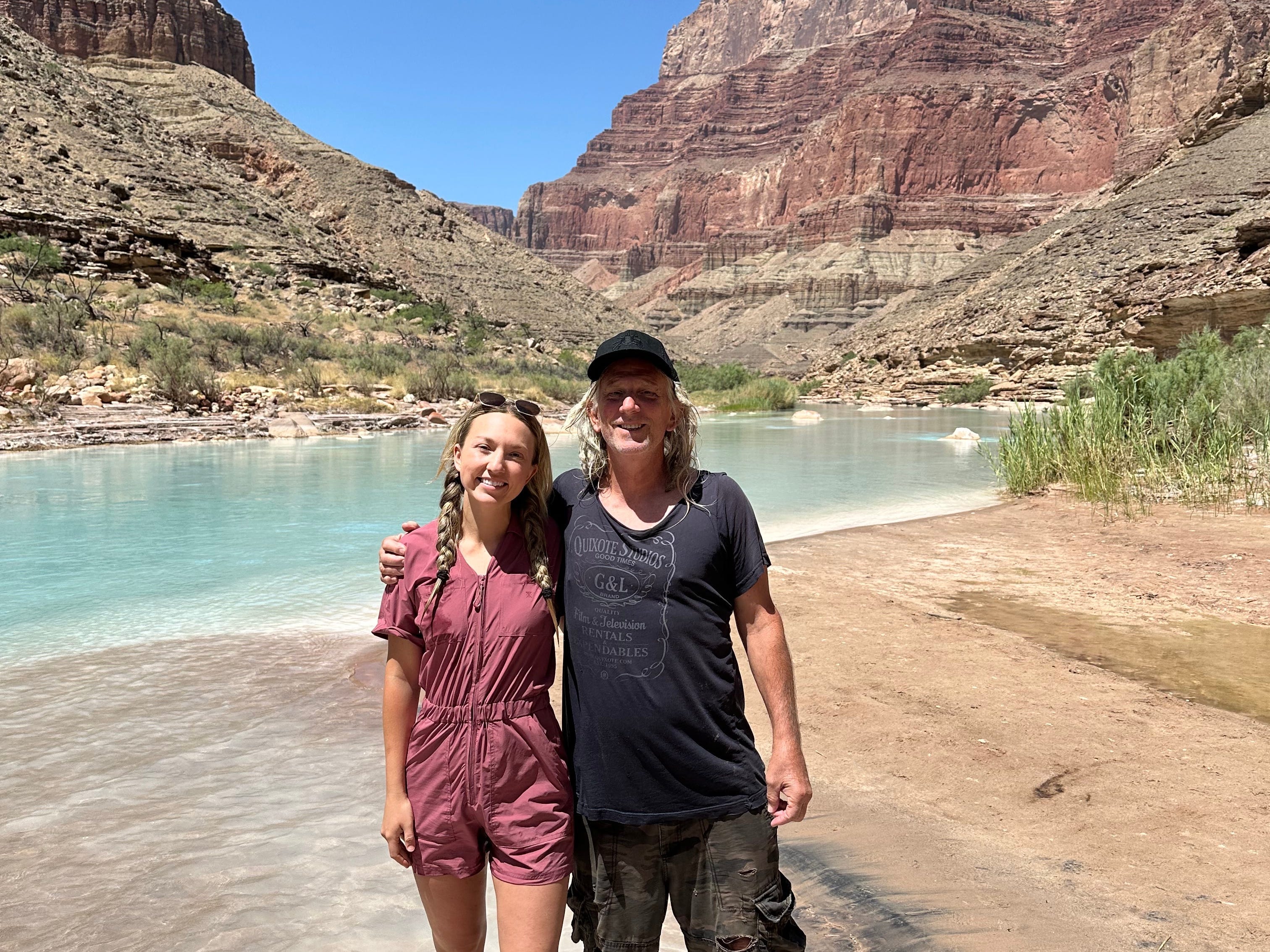 Chloe and her dad pose for a photo near a lake with large rock formations behind them.