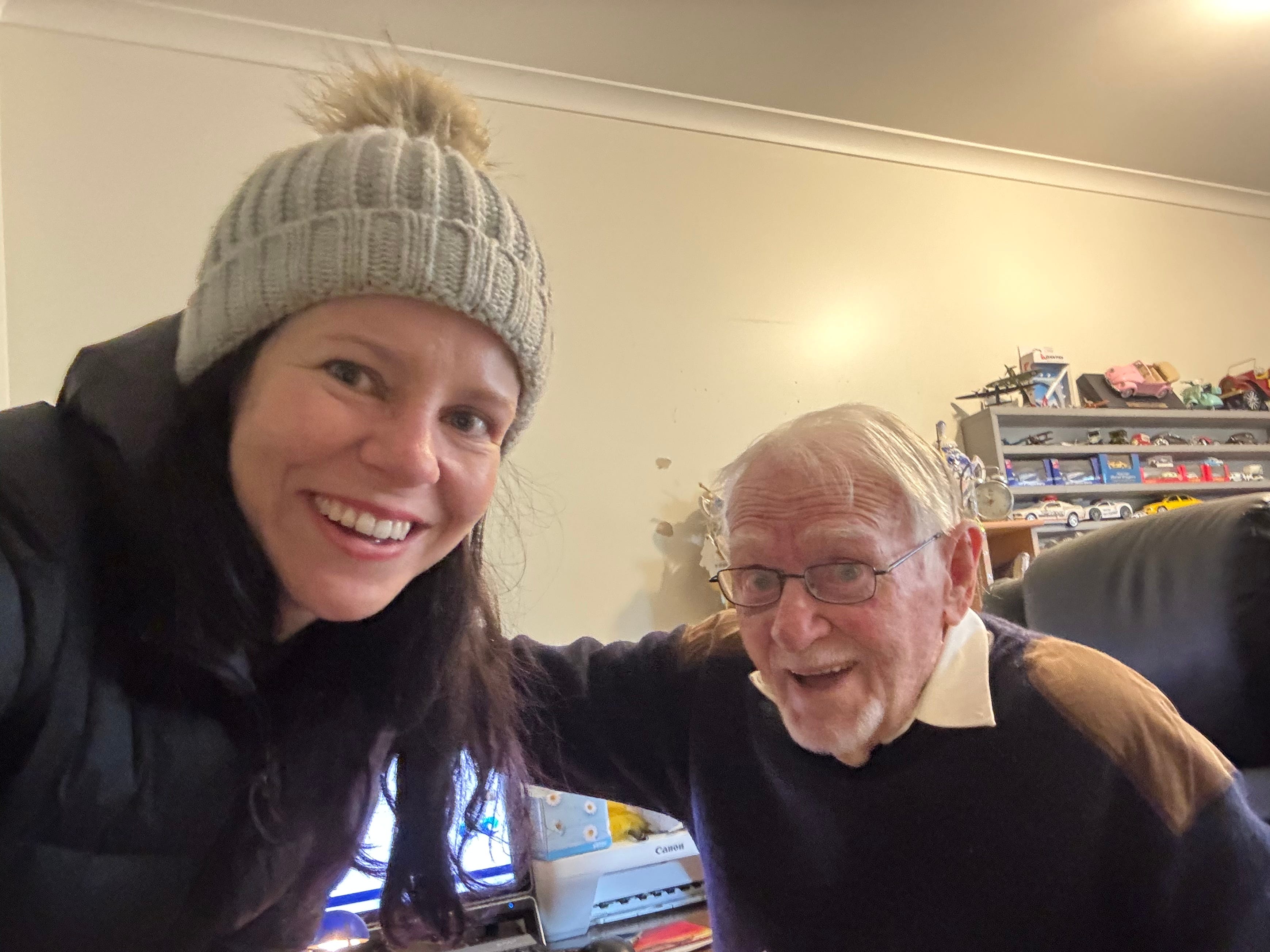 The author visiting with her friend Bryan, who is sitting in a computer chair in front of a desk. They are smiling and hugging.