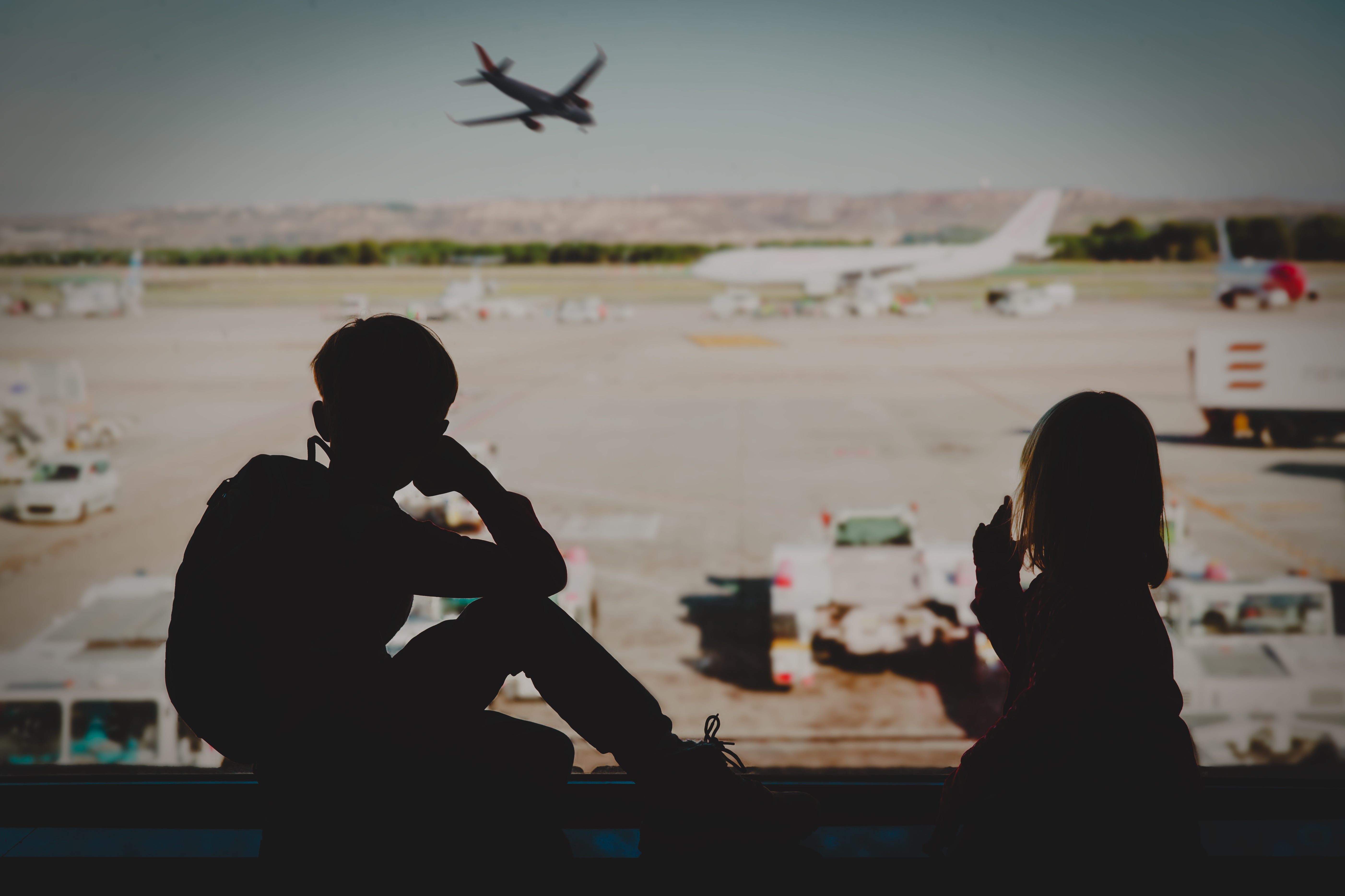 Two kids look out the window on an airport.