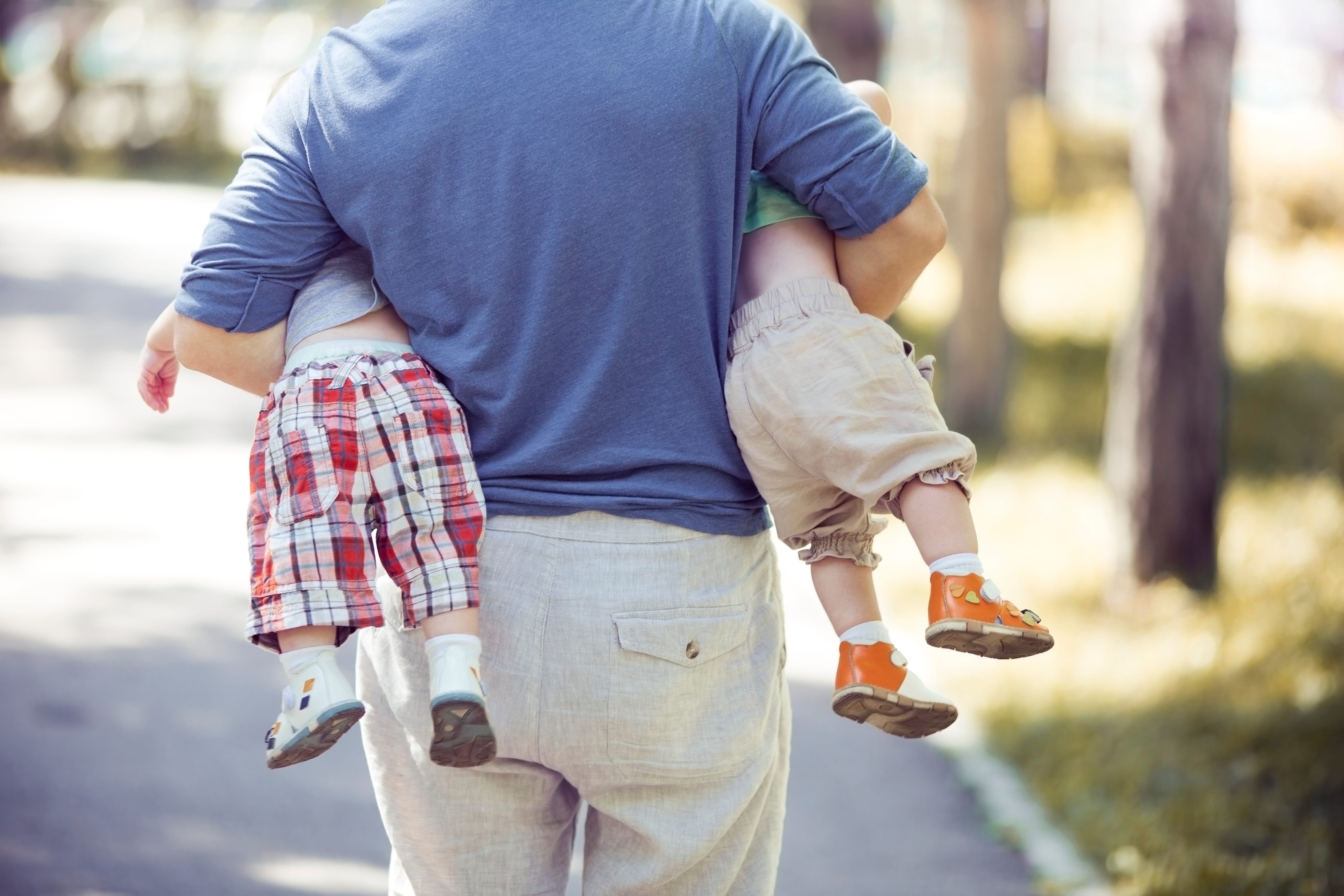 Father is carrying two sons. Back view