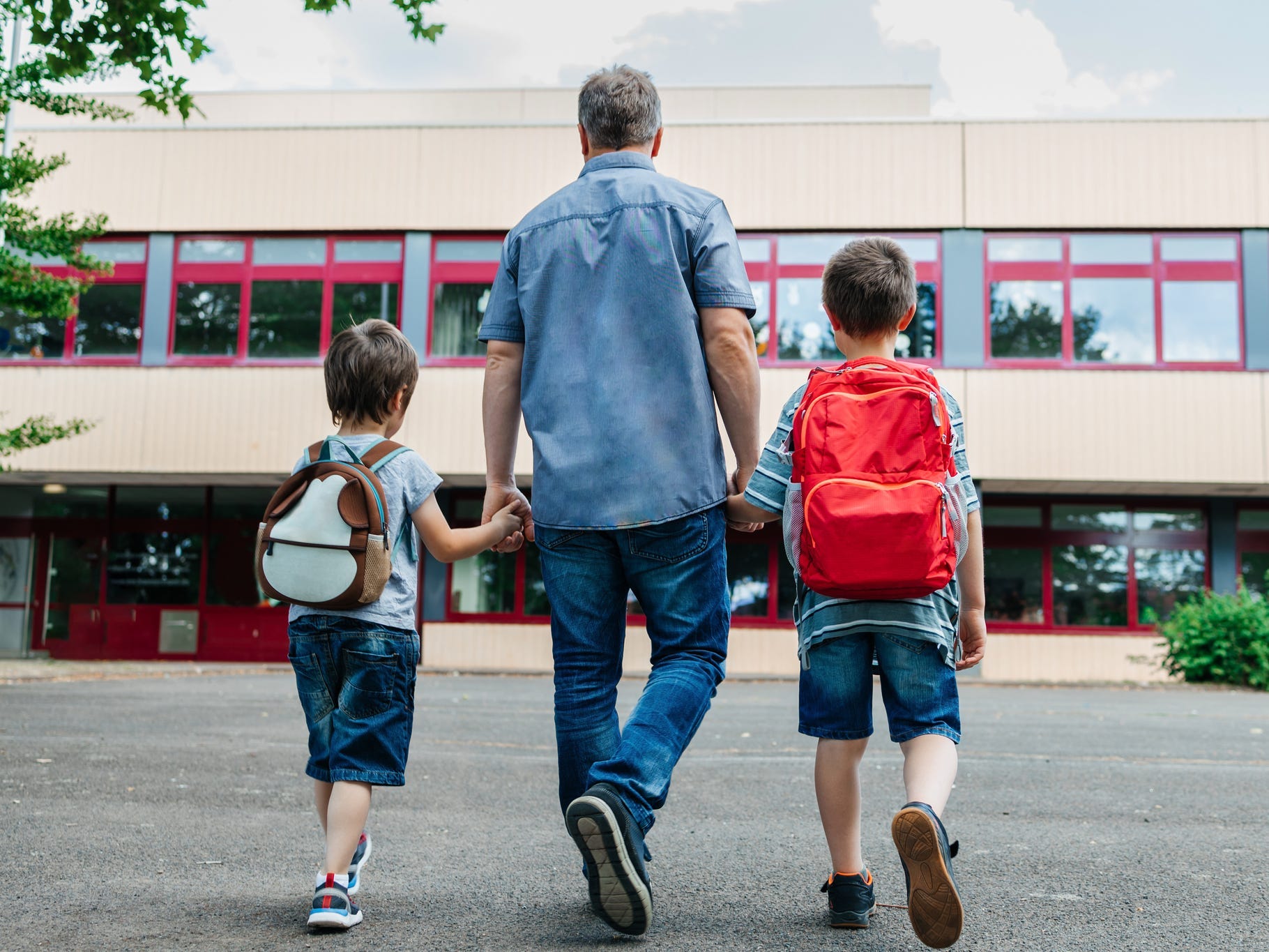 View from the back of a dad holding his sons' hands as they walk to school