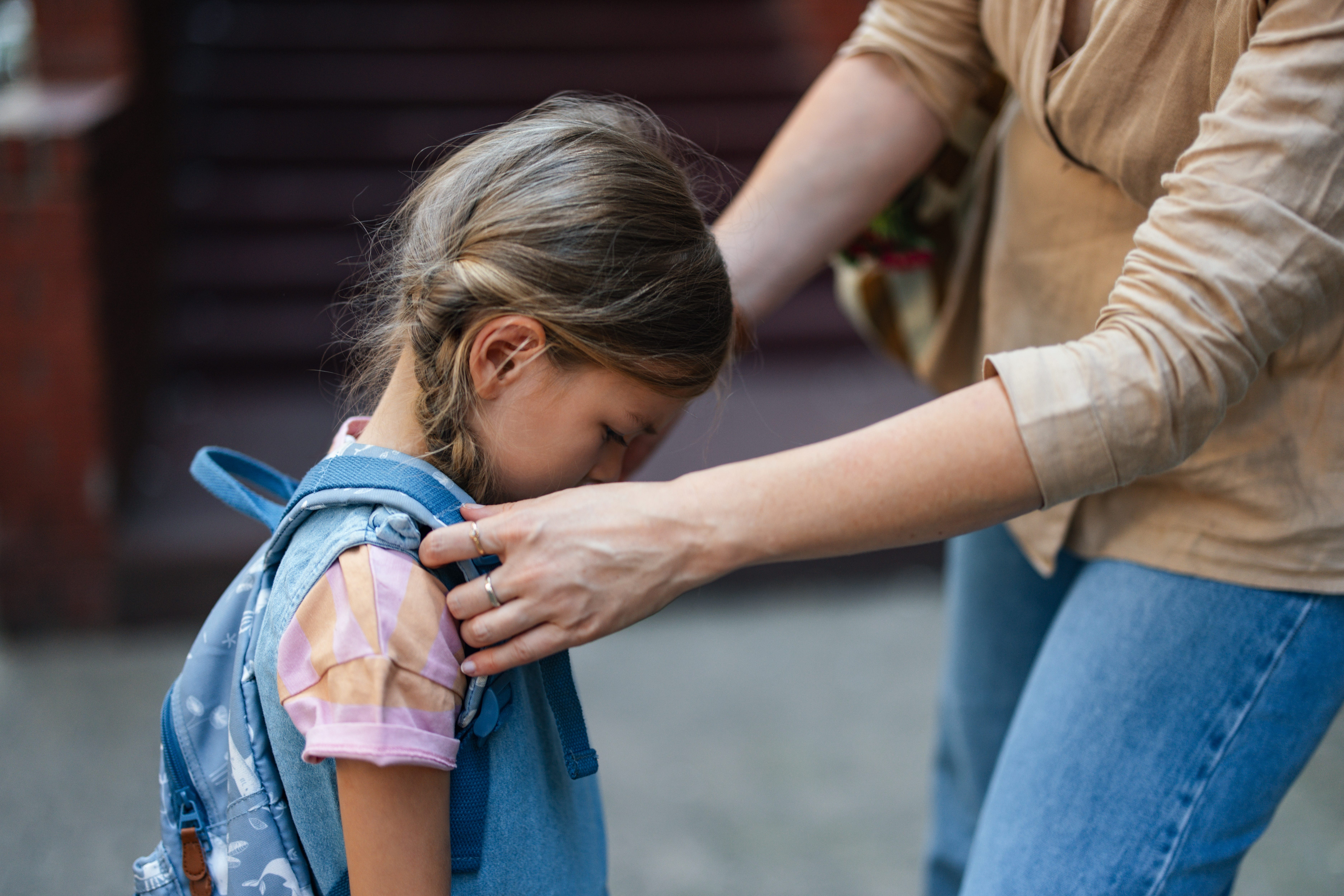 A woman adjusts a backpack on a small child who looks to be upset.