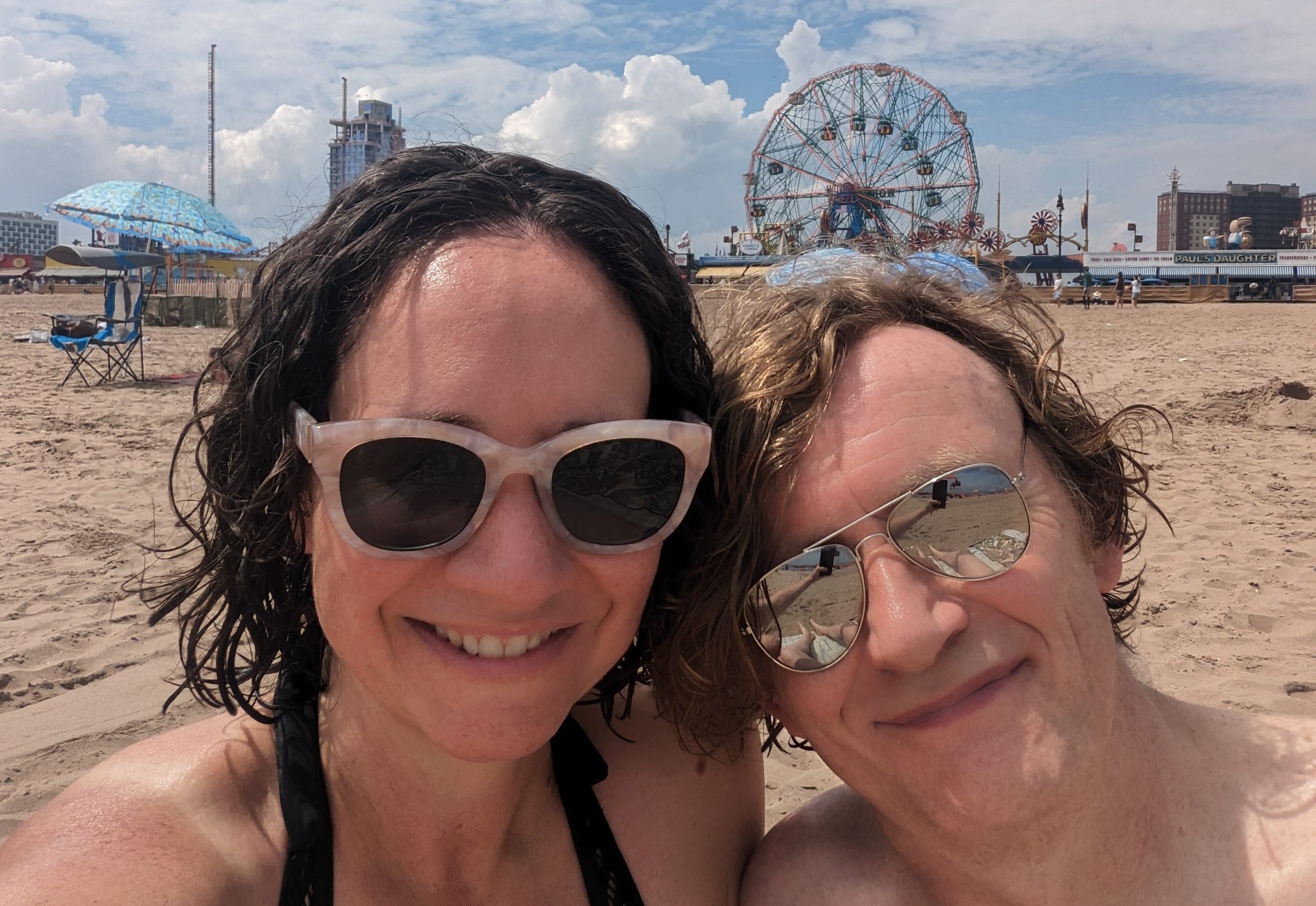 A couple wearing sunglasses poses in the sand at Coney Island.