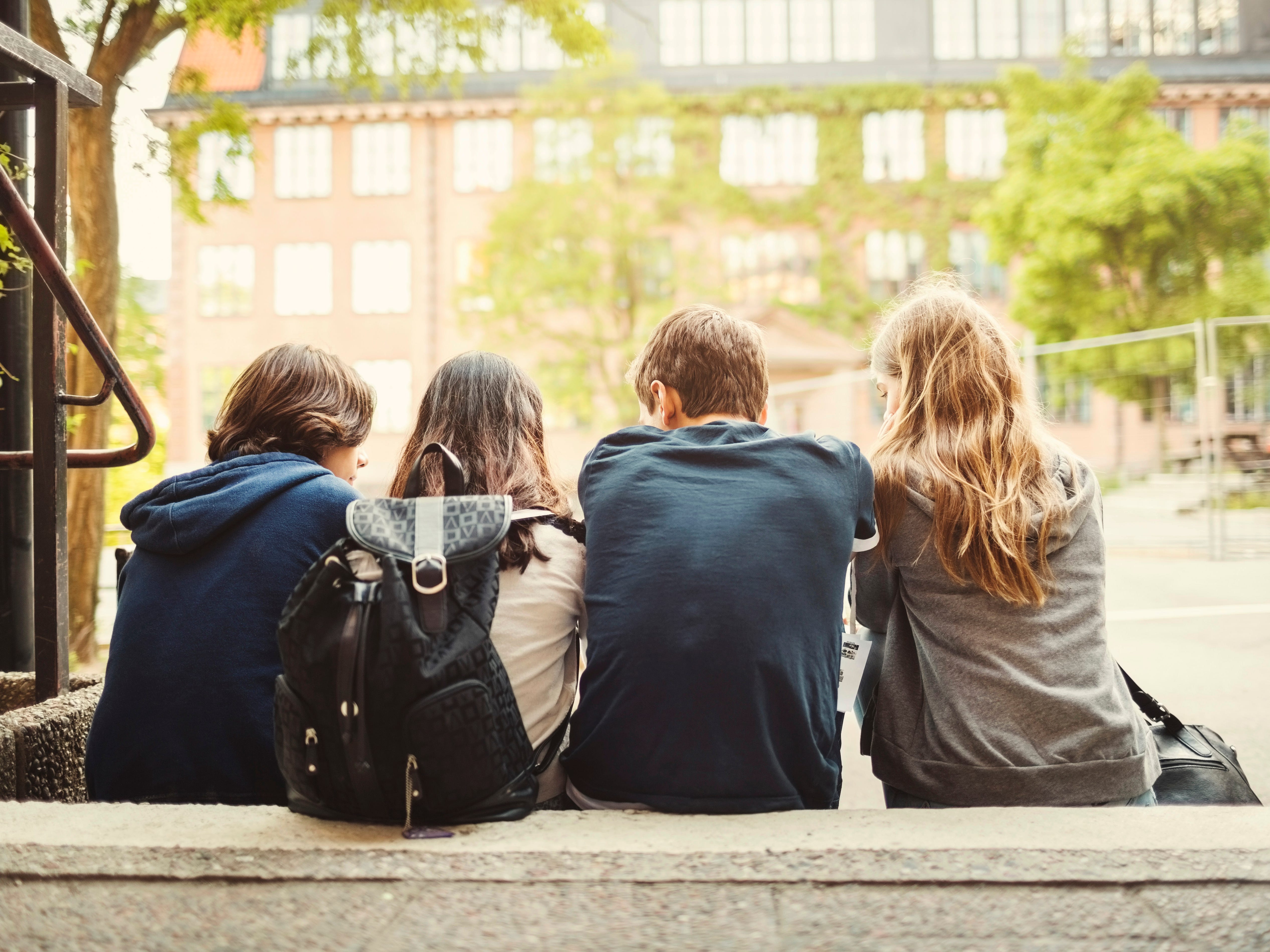 Four teenagers sitting on steps chatting, their back to the camera