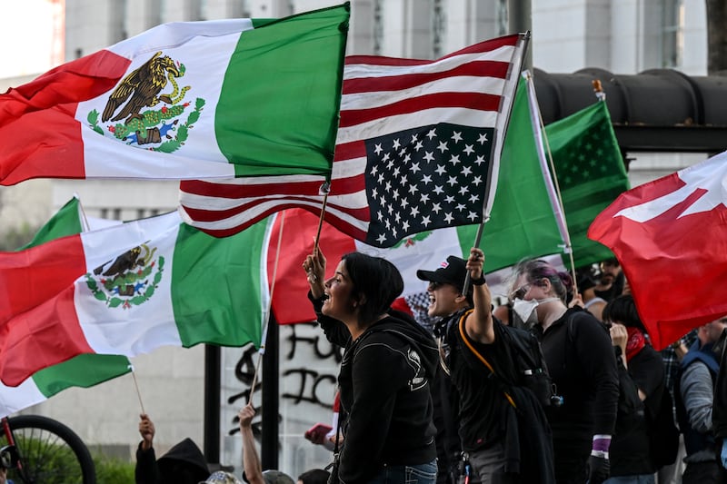 People wave Mexican, U.S. and upside-down U.S. flags as they protest against federal immigration operations near Los Angeles City Hall on June 11, 2025.