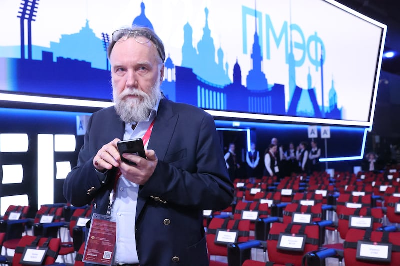 A man with a long beard taps on his phone in front of a sign in Russian.