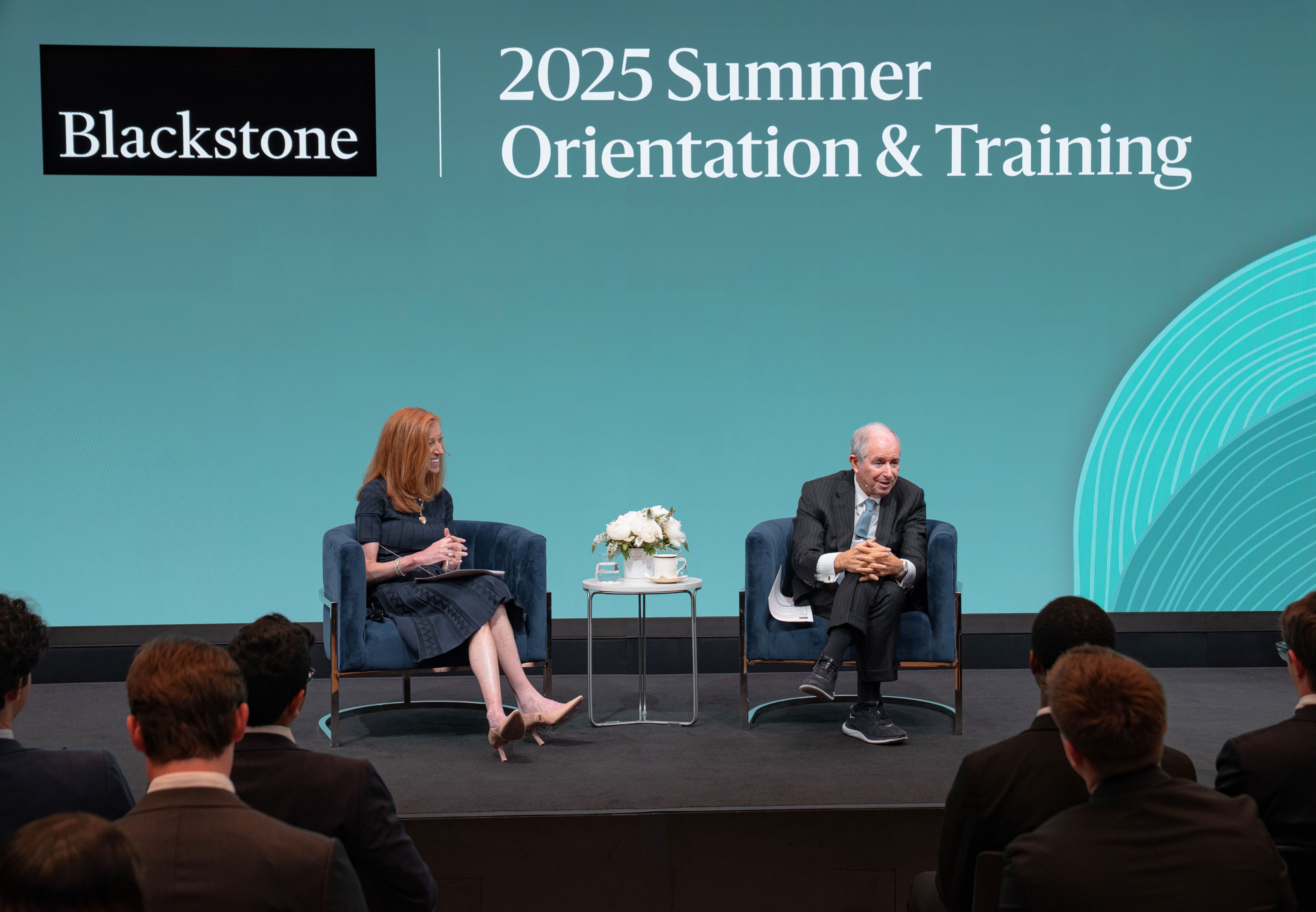 Paige Ross and Steve Schwarzman sit in front of a Blackstone-branded screen, while speaking to summer analysts.