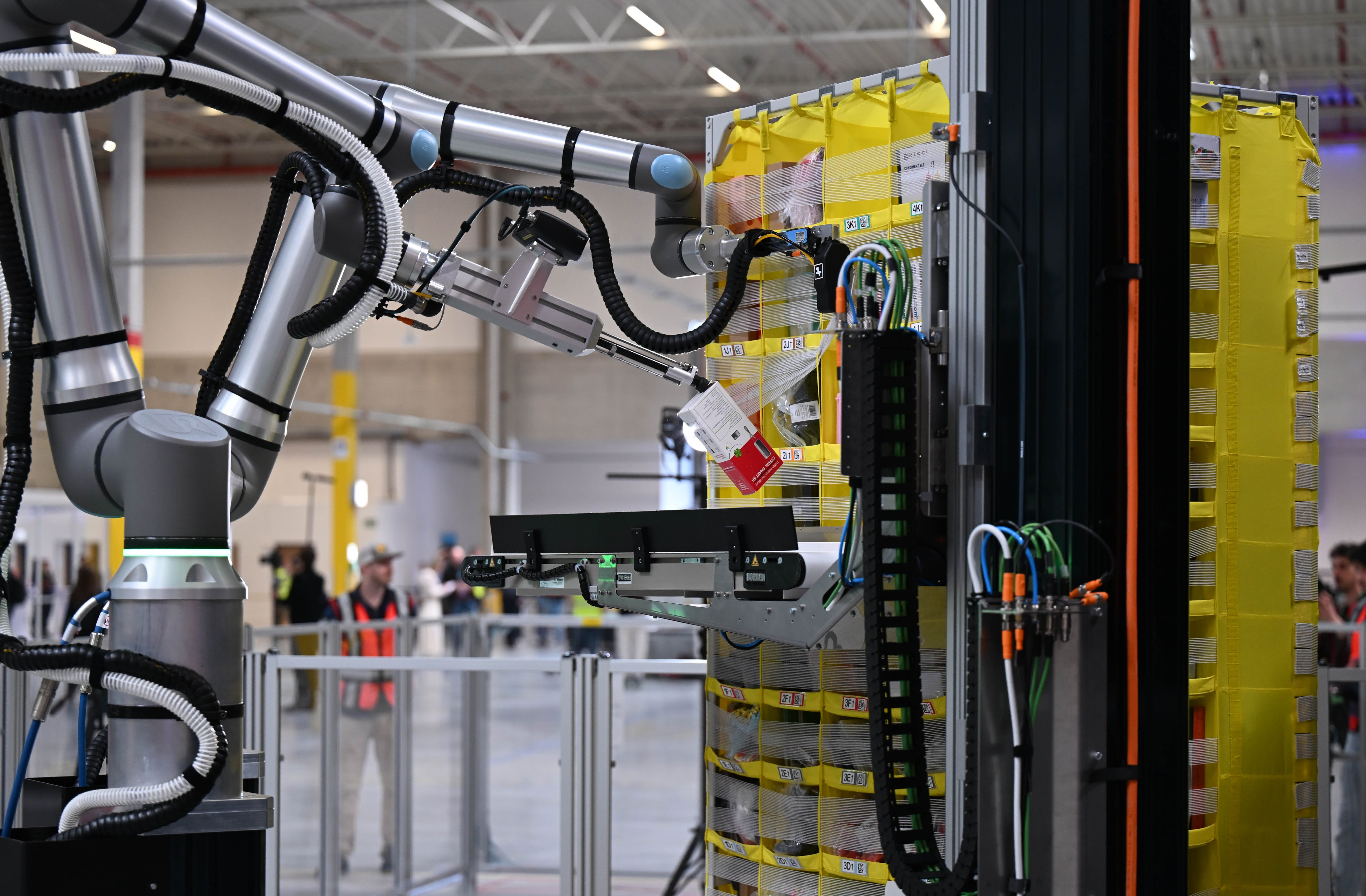 A gripper arm of the Vulcan robot picks up a product from an Amazon mobile warehouse shelf.
