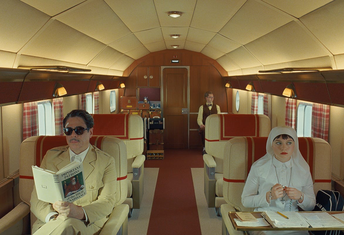 A still of "The Phoenician Scheme" showing Benicio Del Toro, Michael Cera and Mia Threapleton sitting seperately on a plane.