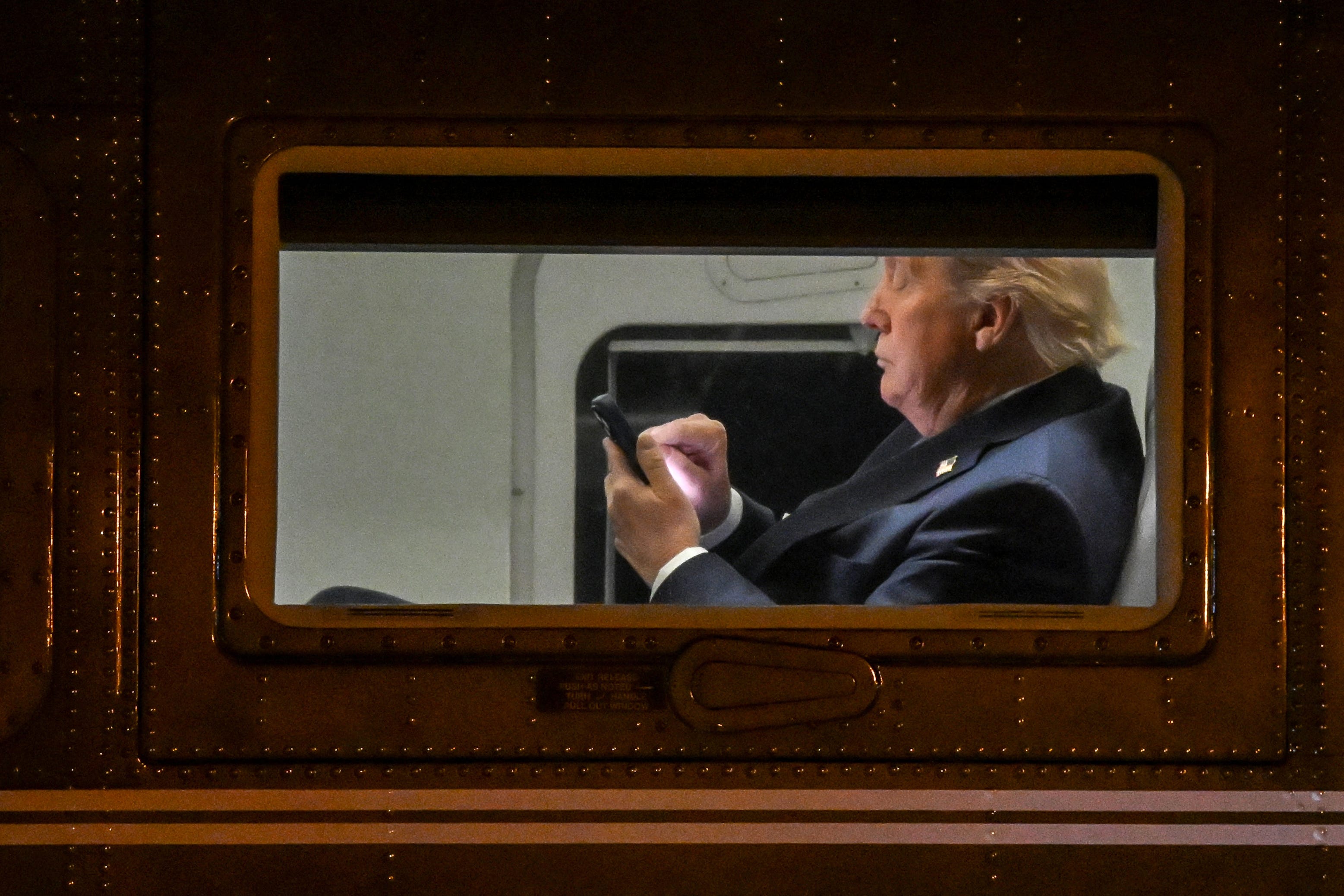Trump aboard Marine One typing on his cellphone, pictured from the side.