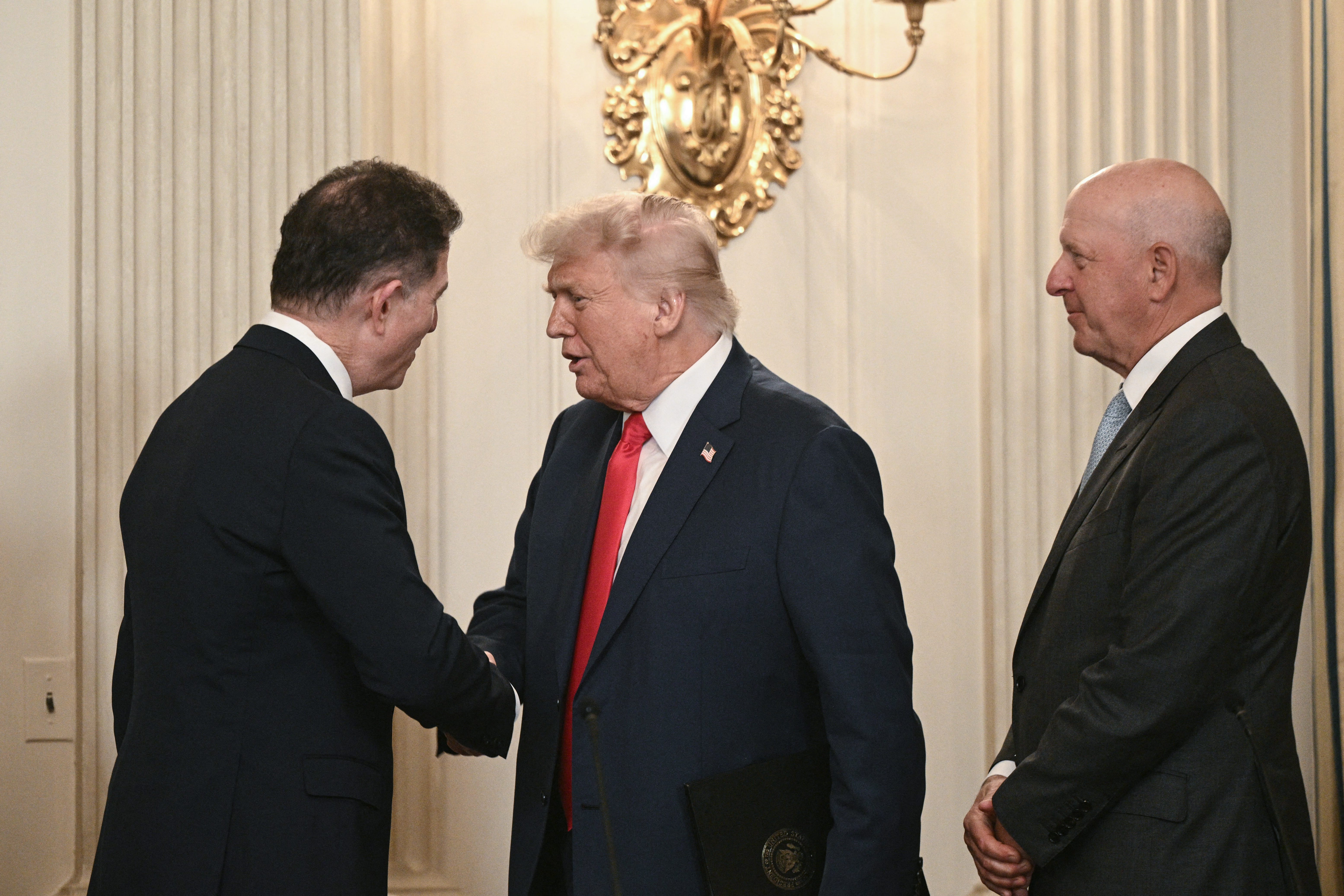 US President Donald Trump shakes hands with Dell Technologies CEO Michael Dell (L) as Goldman Sachs CEO David Solomon (R) looks on