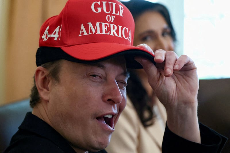 Elon Musk smirks while wearing a cap with the words "Gulf of America" as he attends a cabinet meeting held by President Donald Trump at the White House.
