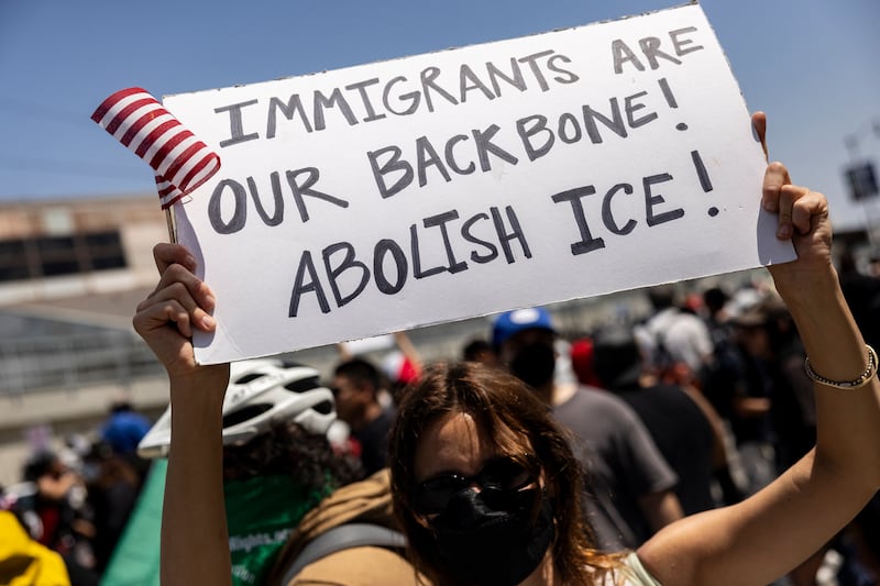 A demonstrator holds a poster reading "Immigrants are our backbone! Abolish Ice!" in front of National guards during clashes with law enforcement in front of the federal building during a protest following federal immigration operations, in Los Angeles, California on June 8