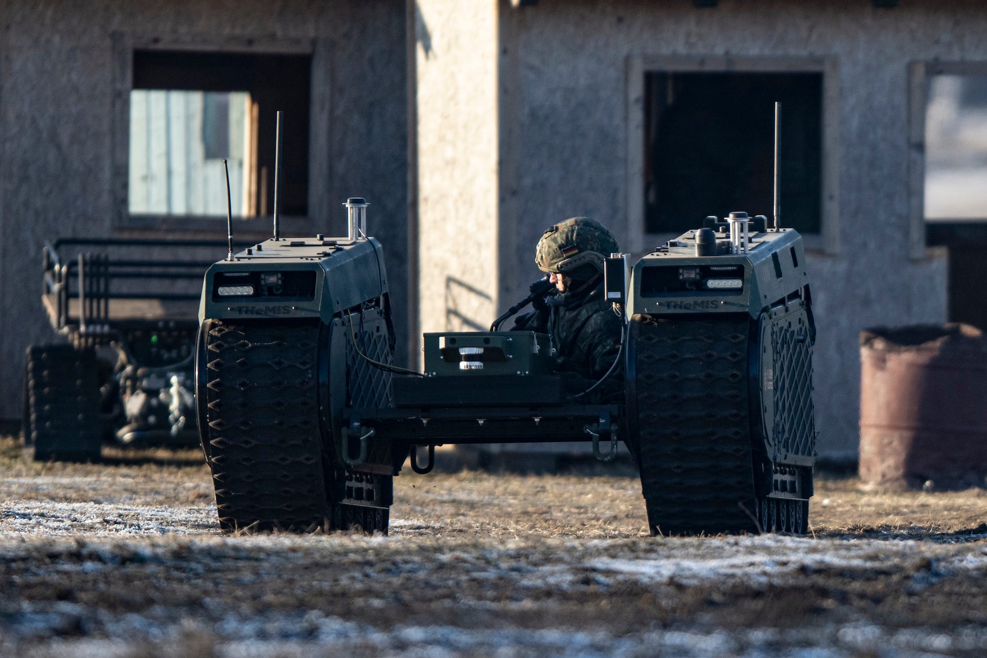 A man in a camouflage helmet sits on a caged rack between two tracks