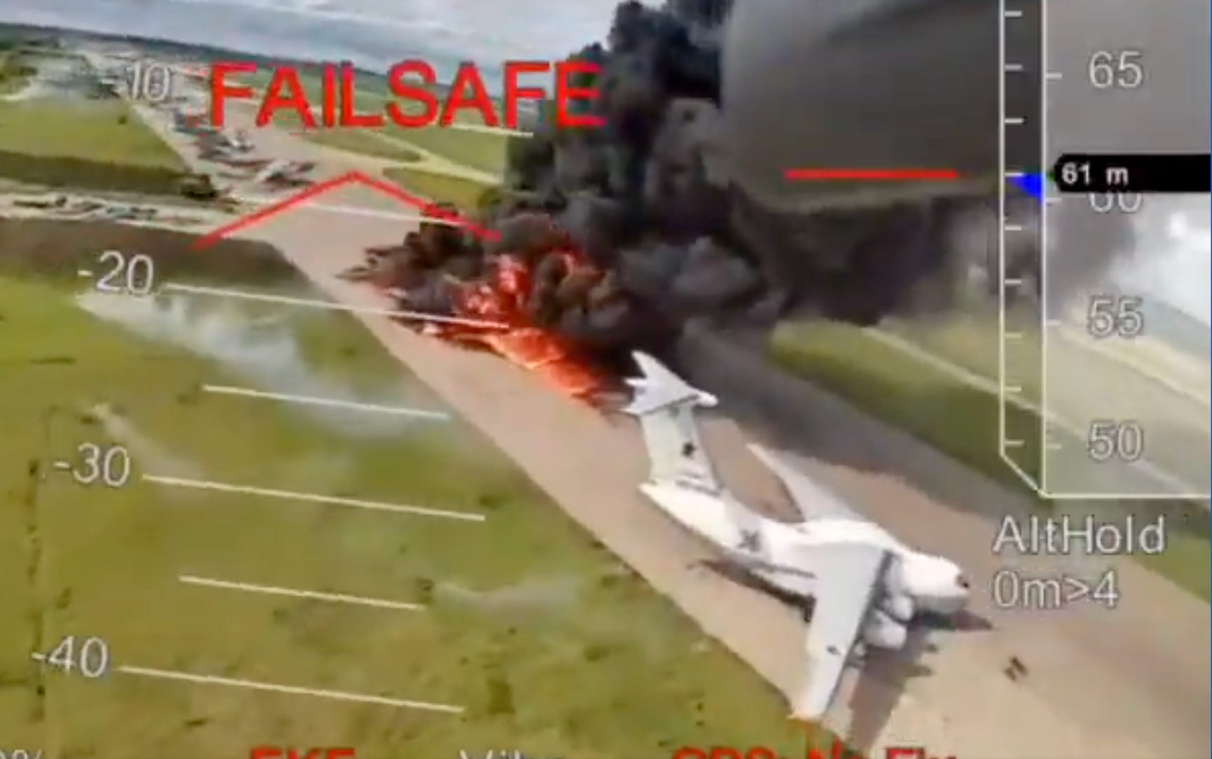 A still from video footage shows a large fire with black smoke beside a white plane on a runway surrounded by grass