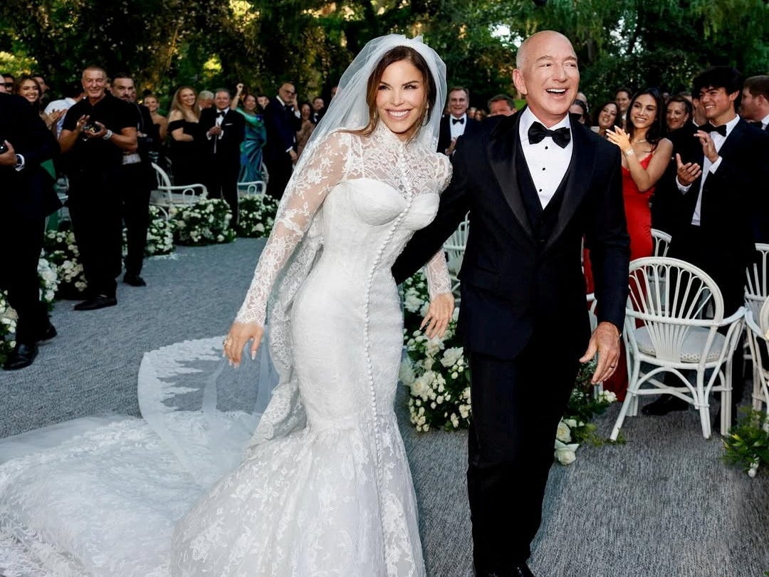 Lauren Sánchez, dressed in a white gown and veil, and Jeff Bezos, wearing a black tuxedo, walk down the aisle after the Venice wedding ceremony.