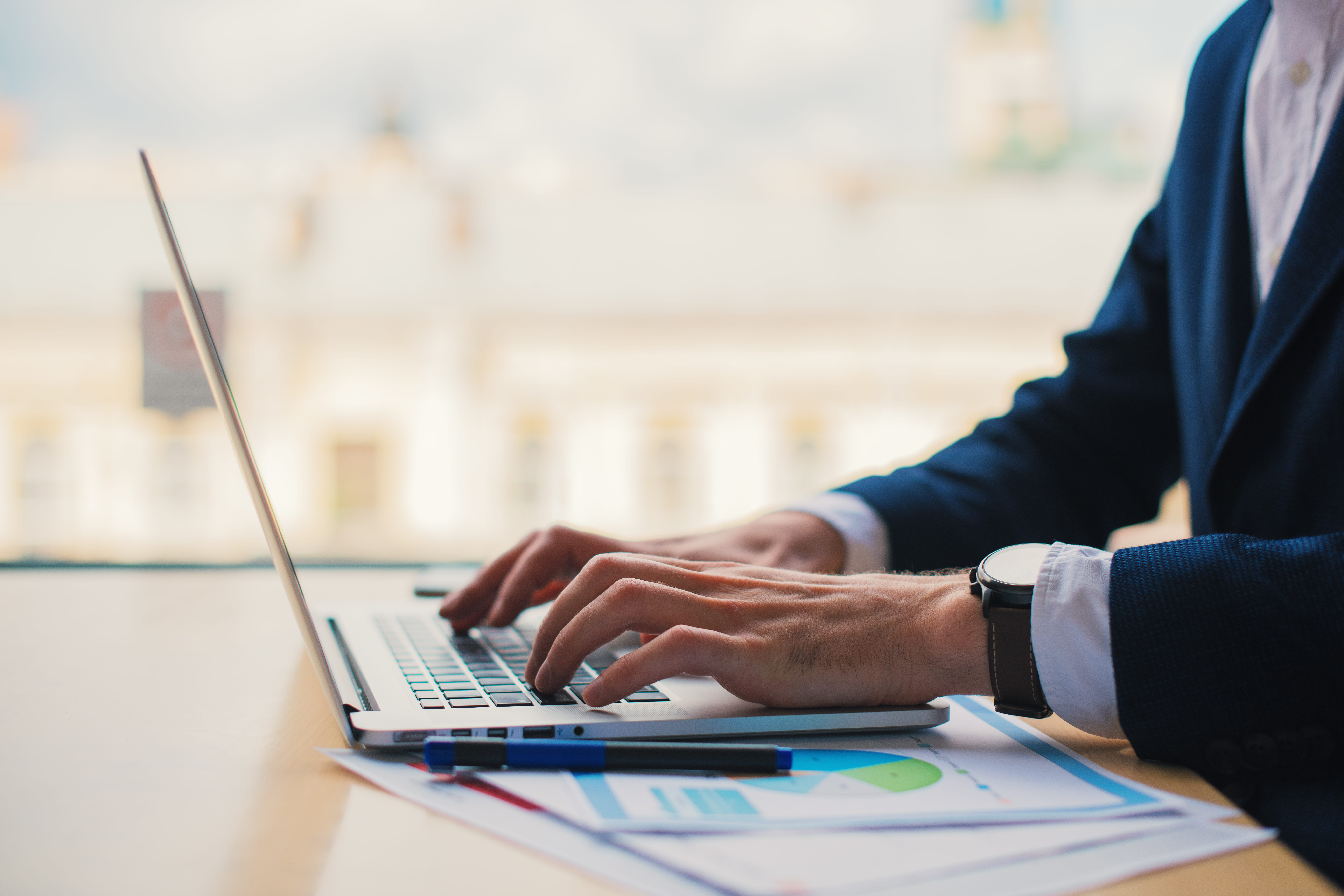 A person in a suit using a laptop on a table with business charts.