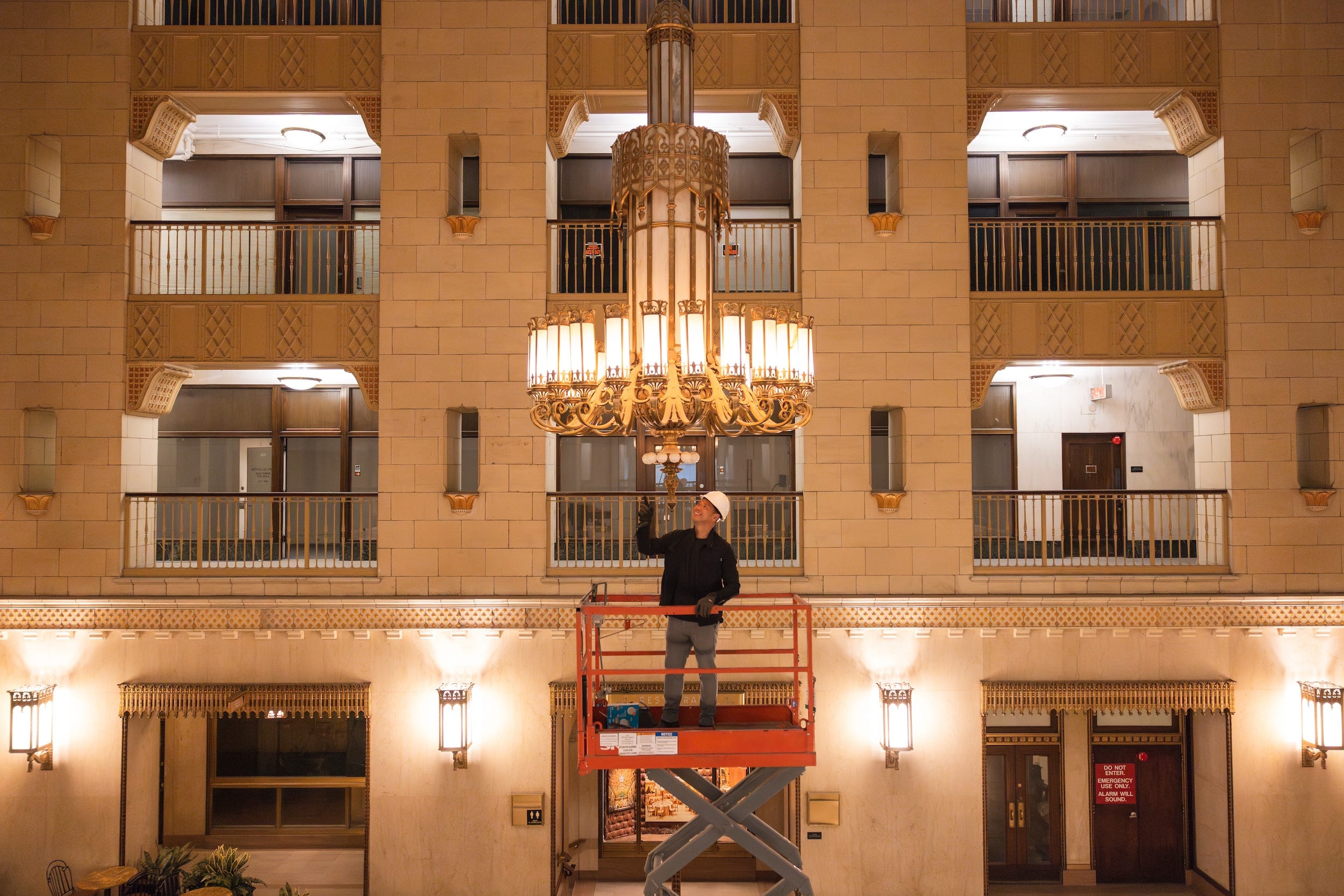 A man standing on a scissor lift beneath a chandelier.