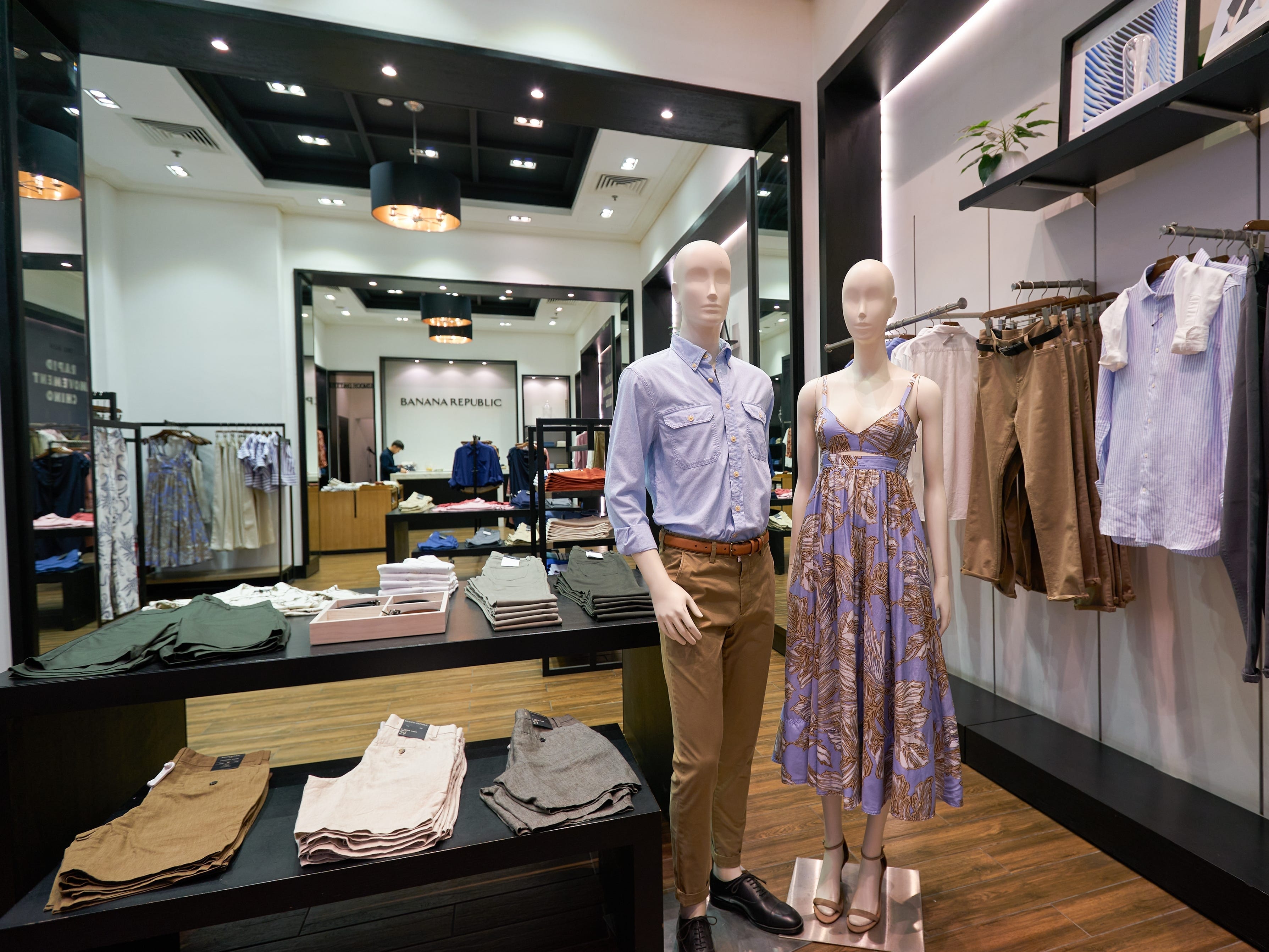 The inside of a Banana Republic store, with a table displaying clothes and two mannequins to the right of the table.