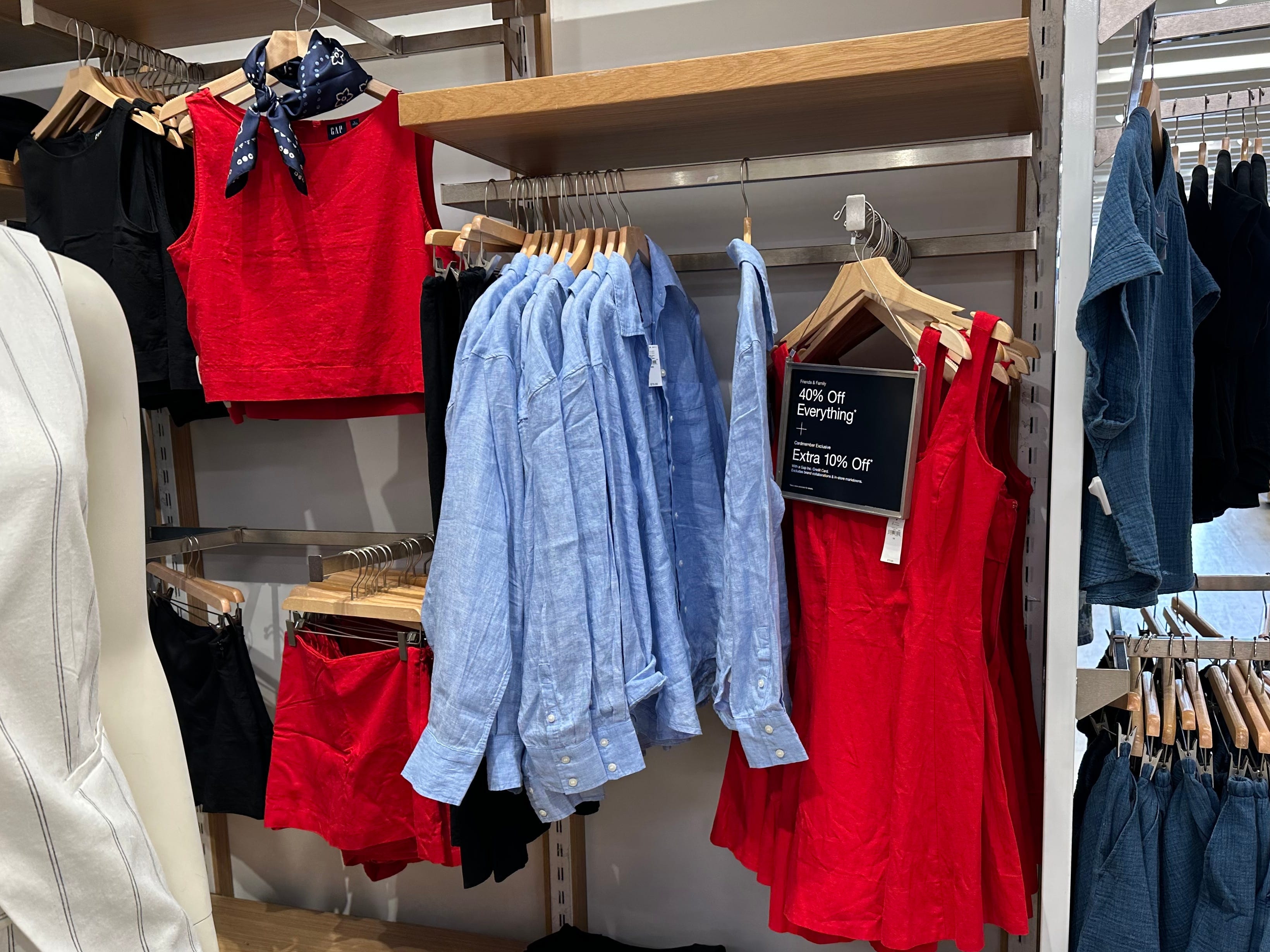 A red top, a red skirt, a blue button-down, and a red dress hanging on the racks at Gap.