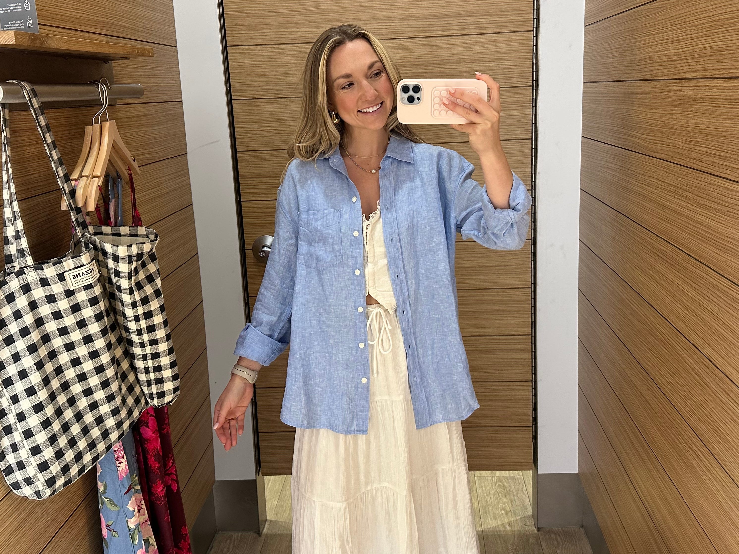 Chloe wears a blue linen button-up shirt over a white top and a long white flowy skirt in a Gap fitting room.