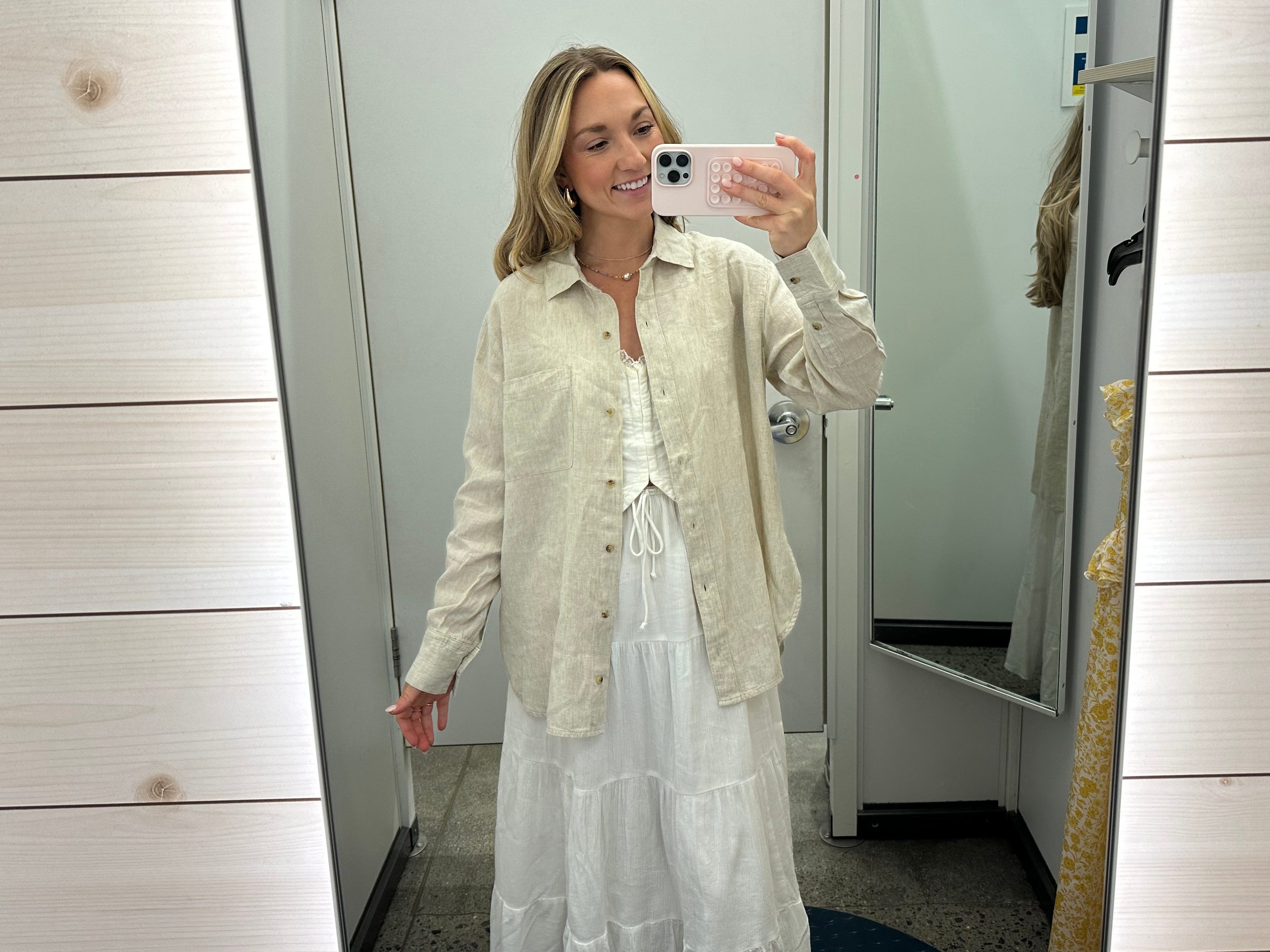 Chloe wears a beige button-up shirt over a white top and a long white flowy skirt in an Old Navy fitting room.
