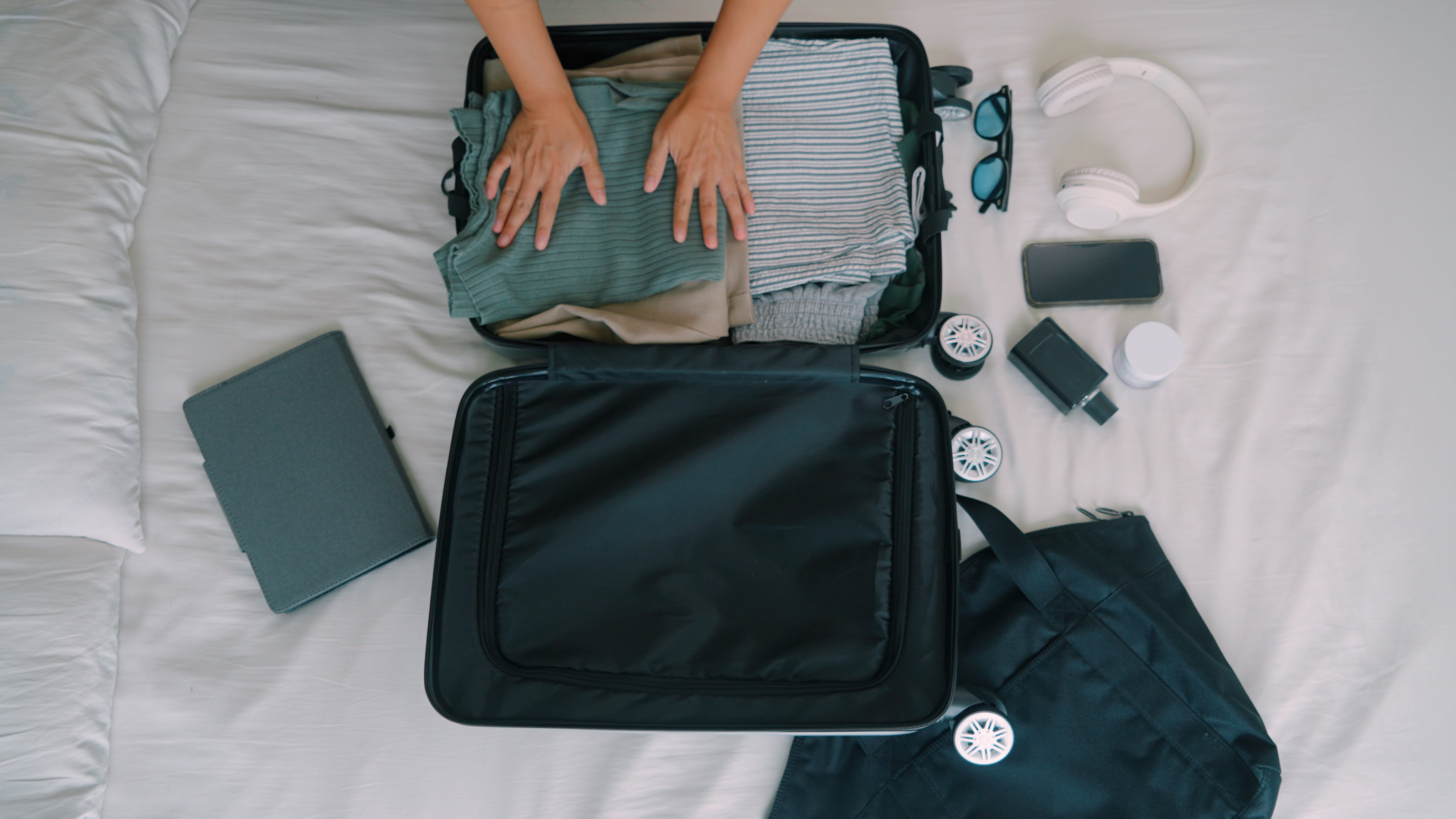 Hands smooth out a pice of clothing inside an open suitcase.