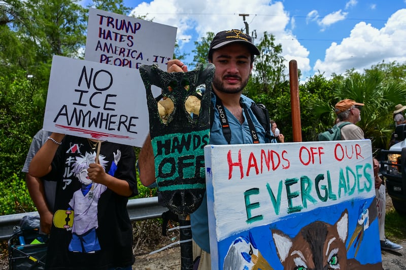Demonstrators hold signs as they protest Trump's visit to a migrant detention center, dubbed