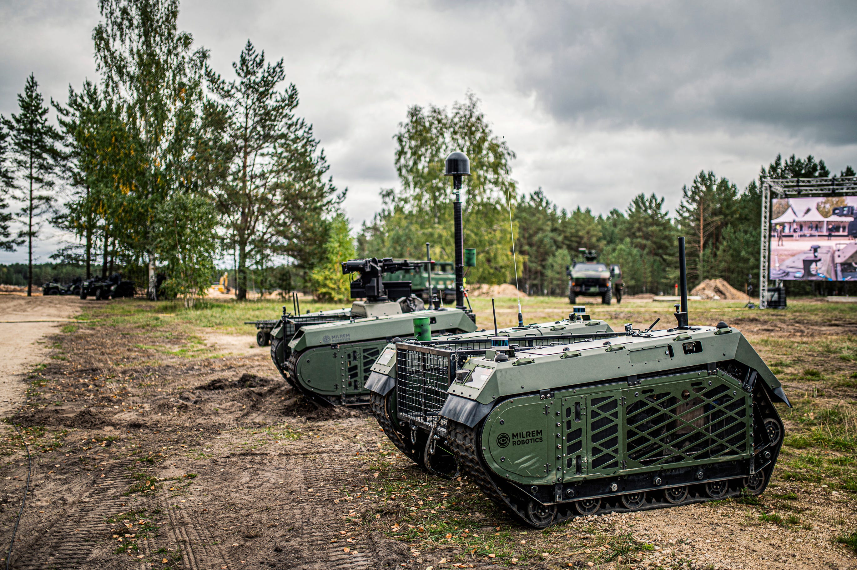 two unmanned ground vehicles on sparse terrain with trees in background