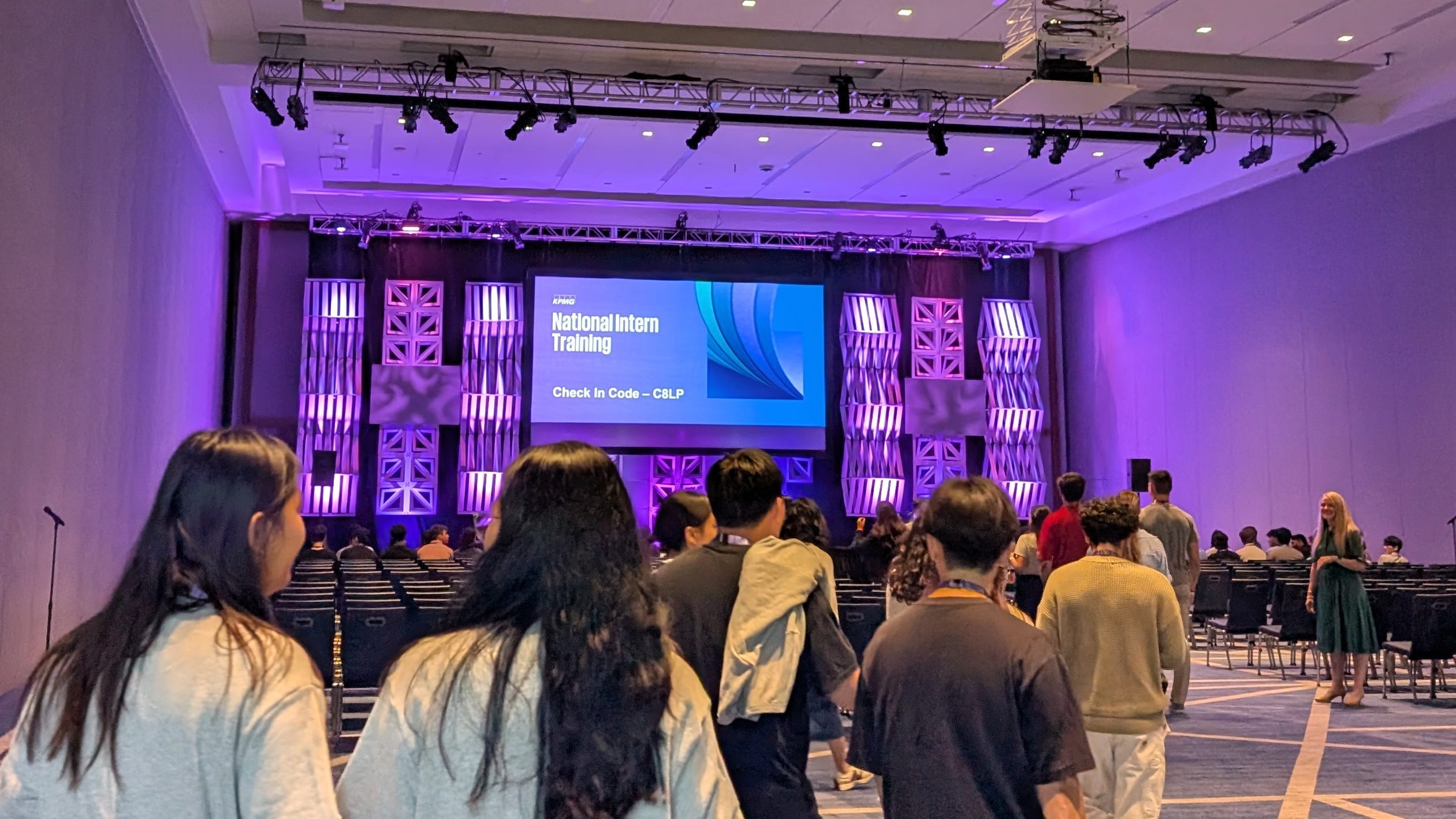 KPMG interns arrive at a welcome event in a hall with a purple screen.