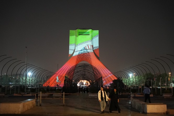 People walk in front of an illuminated monument at the Azadi Square