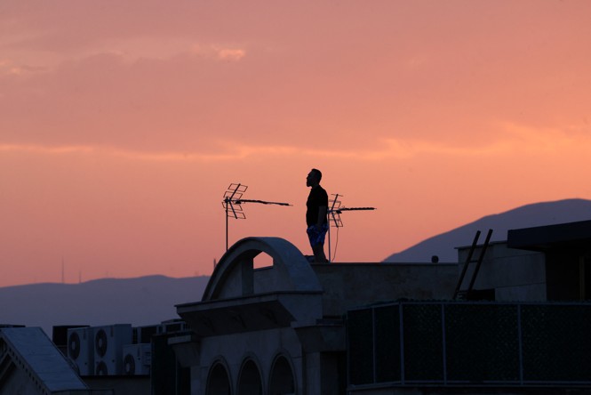 A person silhouetted by a pink sky stands on a roof