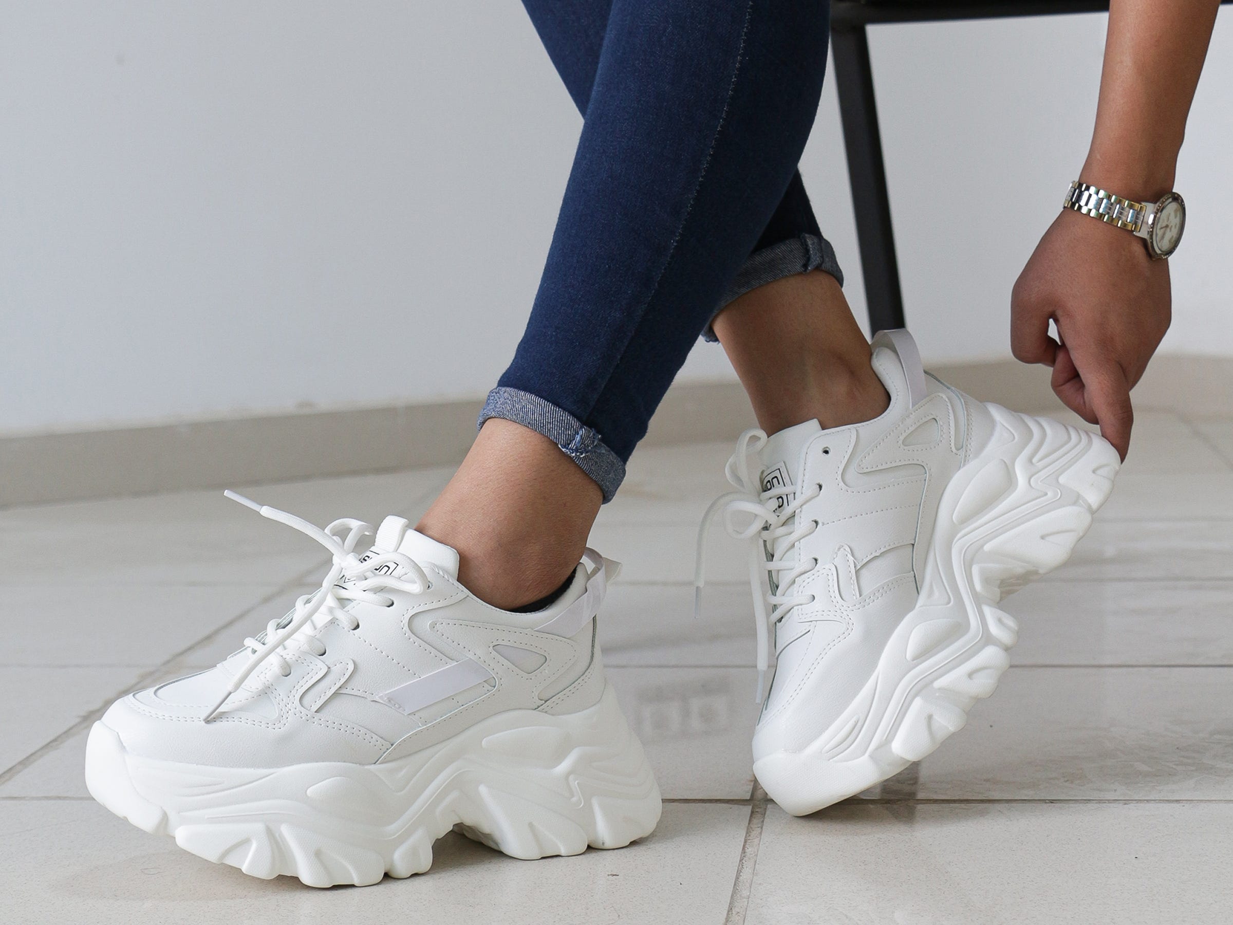 The feet of a woman putting on a pair of white chunky sneakers.