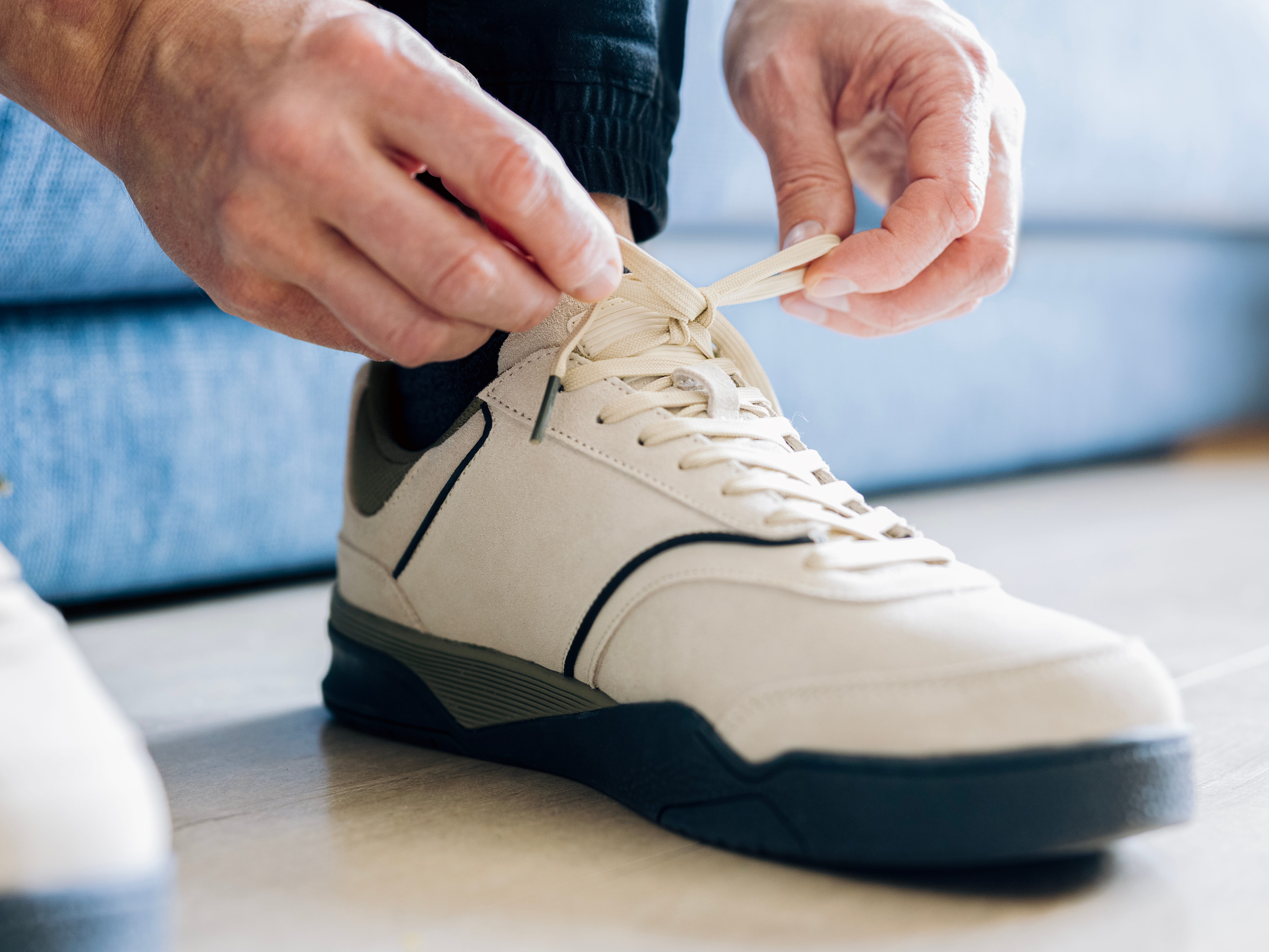 A man tying a pair of white leather sneakers.